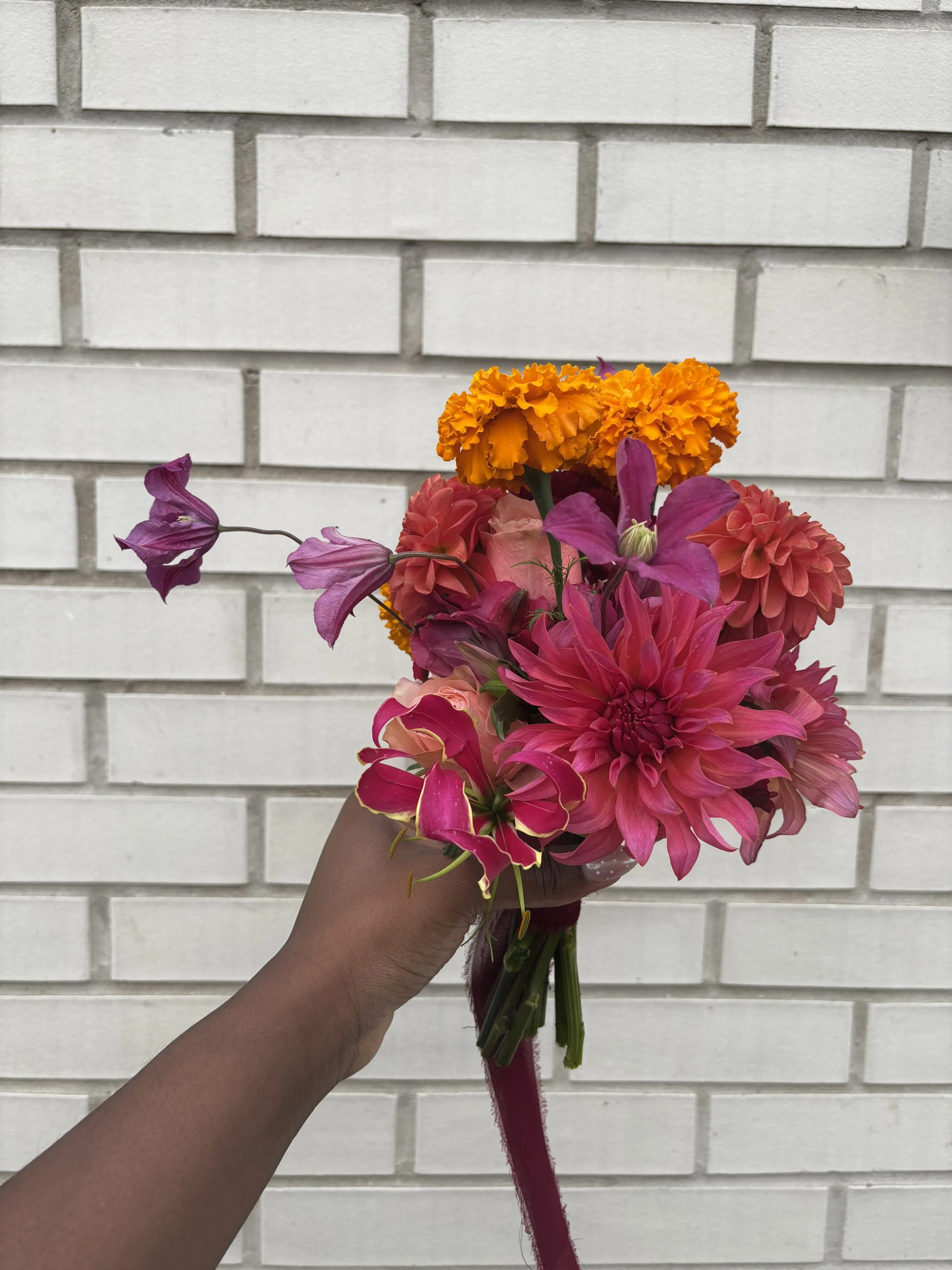 A person holding a bouquet of colorful flowers against a white brick wall.