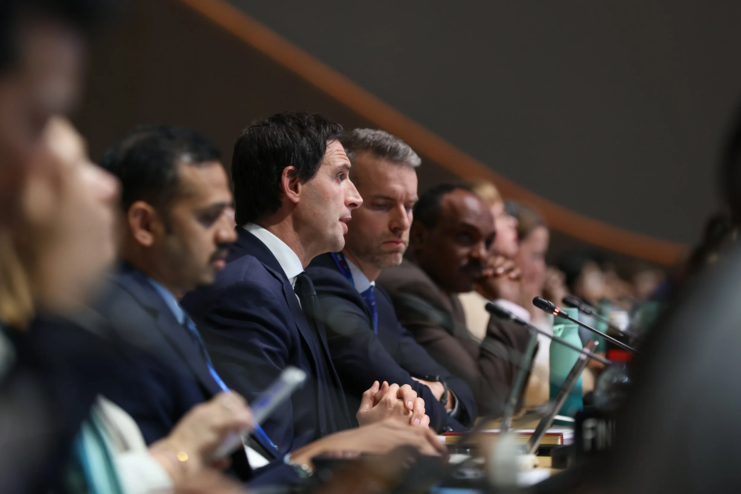 A group of diverse individuals in business attire seated at a conference table, listening attentively during a professional meeting or panel discussion - www.brentkerrigan.com - photo by Kiara Worth
