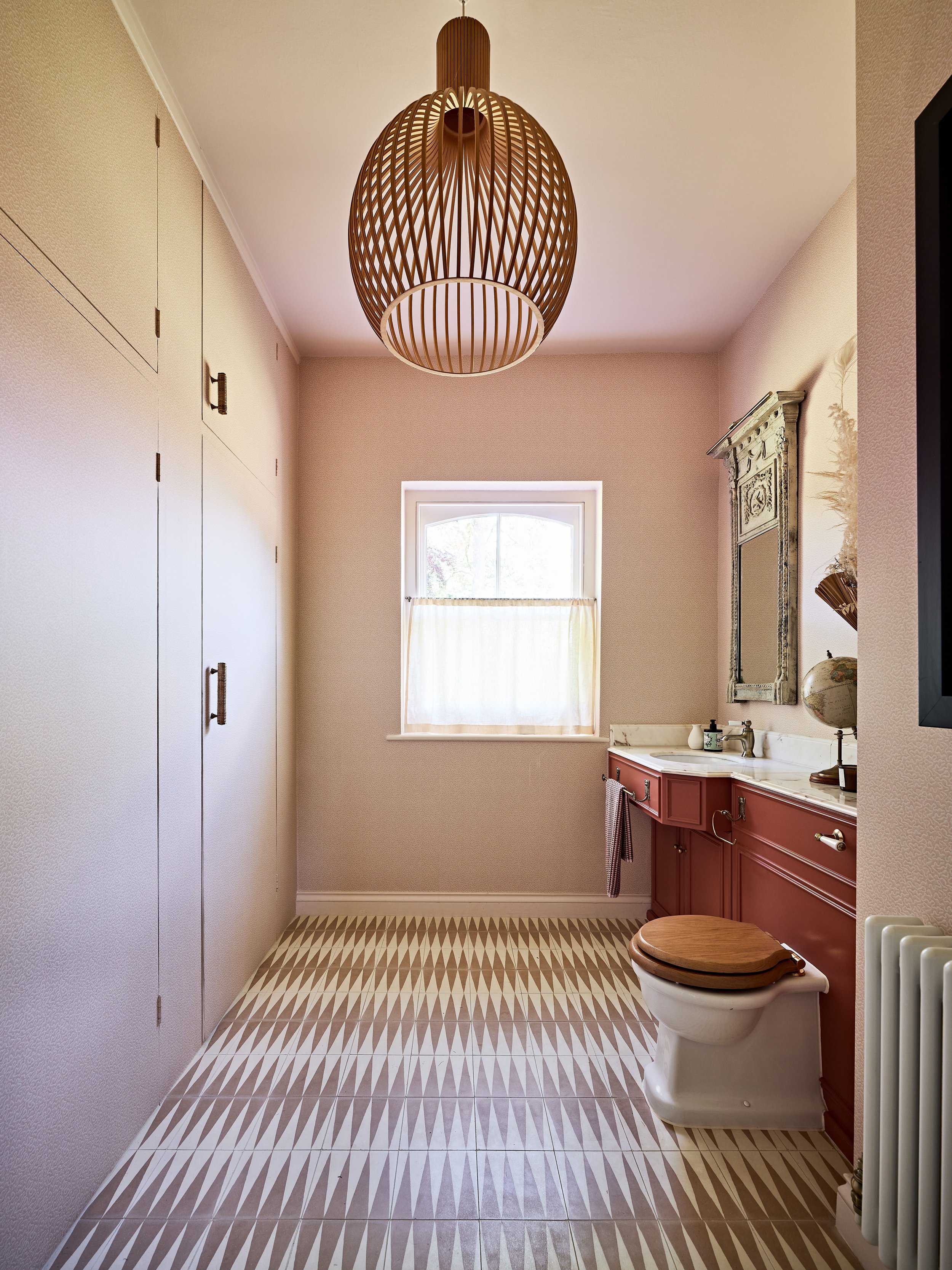 Bathroom with patterned floor tiles, wooden toilet seat, red vanity, ornate mirror, and large hanging light fixture.