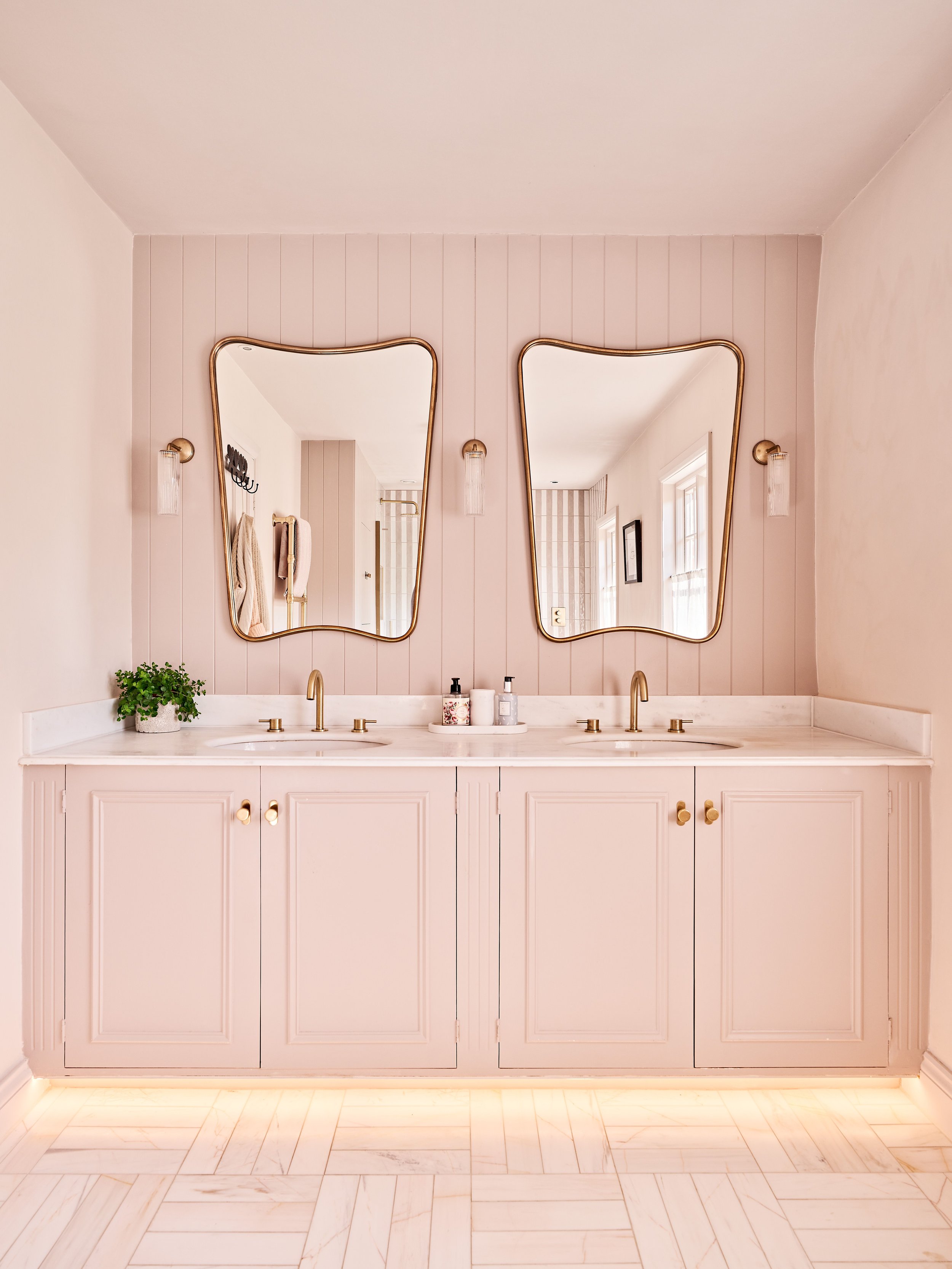 Modern bathroom with pink double vanity, two mirrors, and gold fixtures.