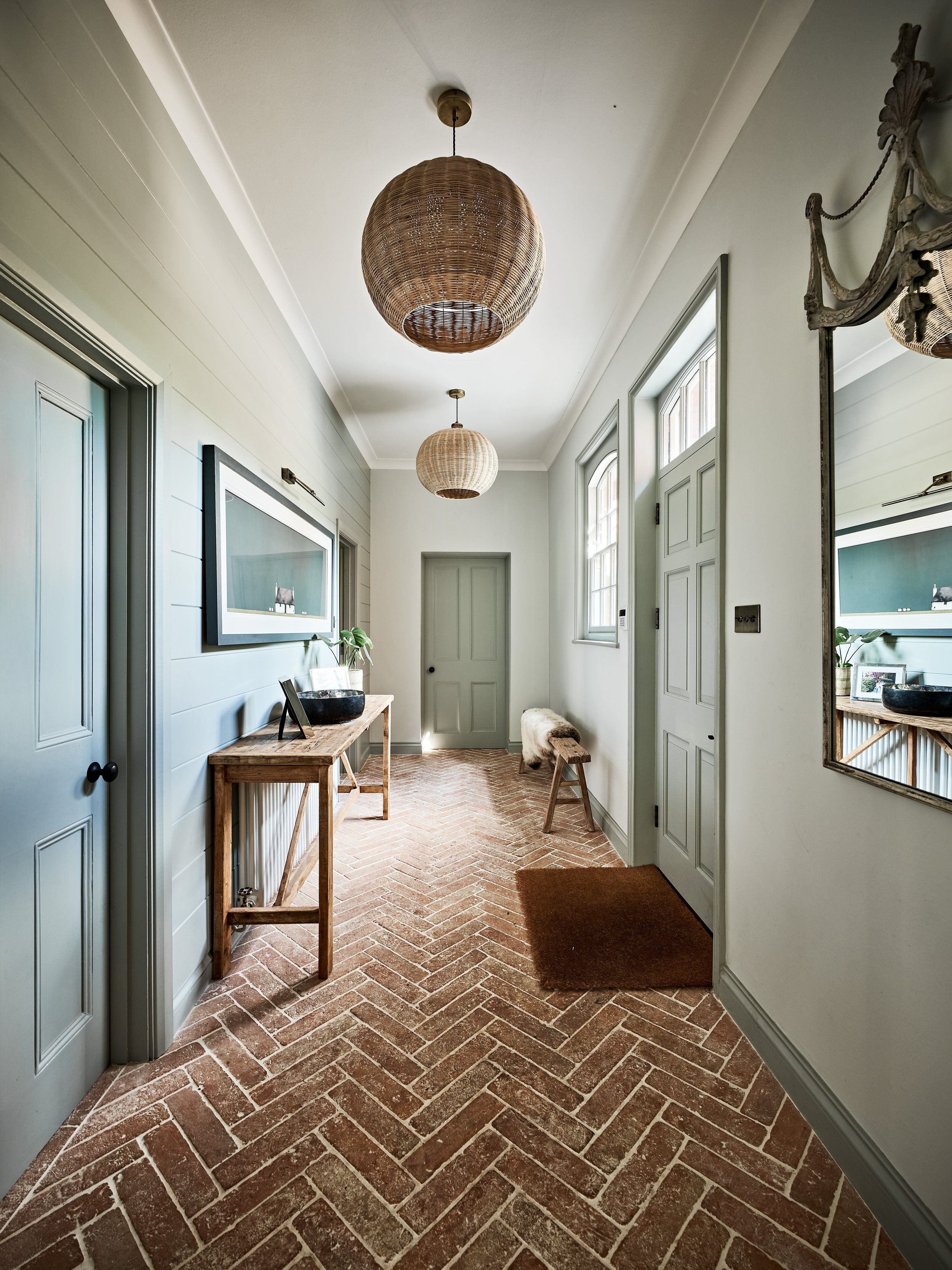 Hallway with brick herringbone floor, wicker light fixtures, wood console table, and wall mirror.
