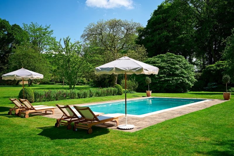Outdoor swimming pool with lounge chairs and umbrellas surrounded by lush greenery.