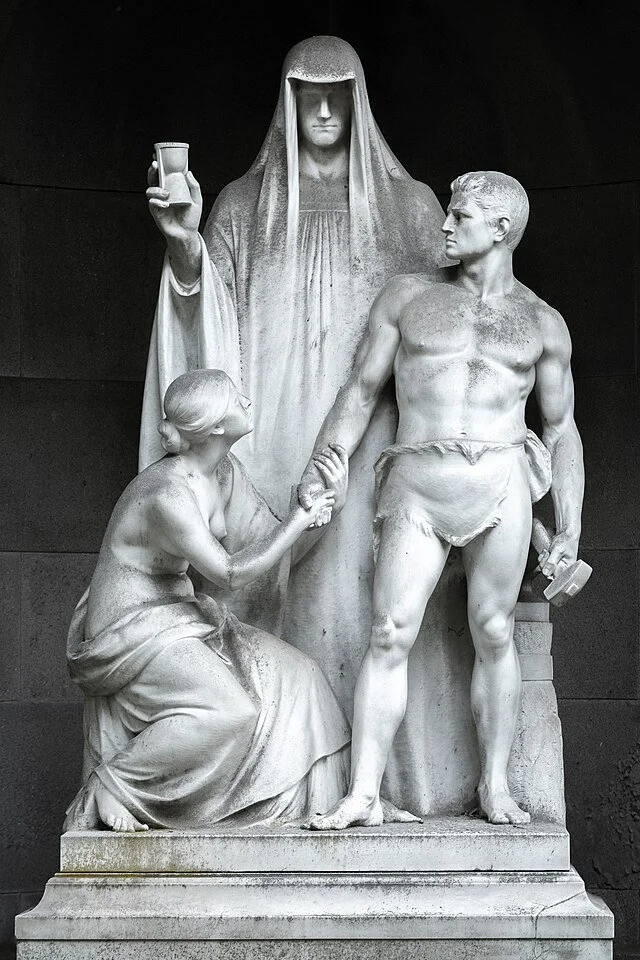 Black and white sculpture depicting a woman seated, a muscular young man holding a dumbbell, and a larger woman standing behind them holding a cup.