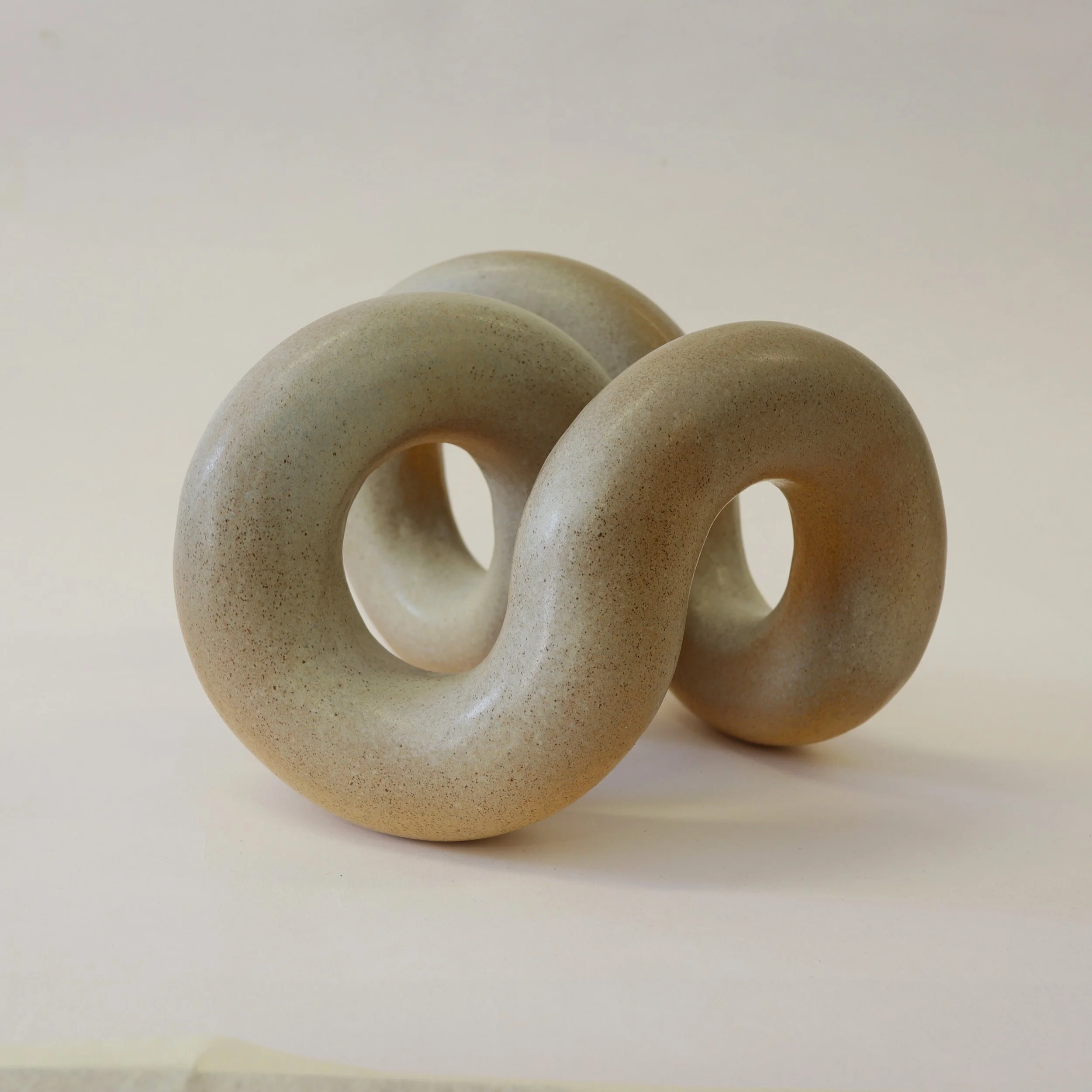 Abstract sculpture resembling a continuous loop or figure-eight shape, made of light-colored material with a smooth, matte surface.
