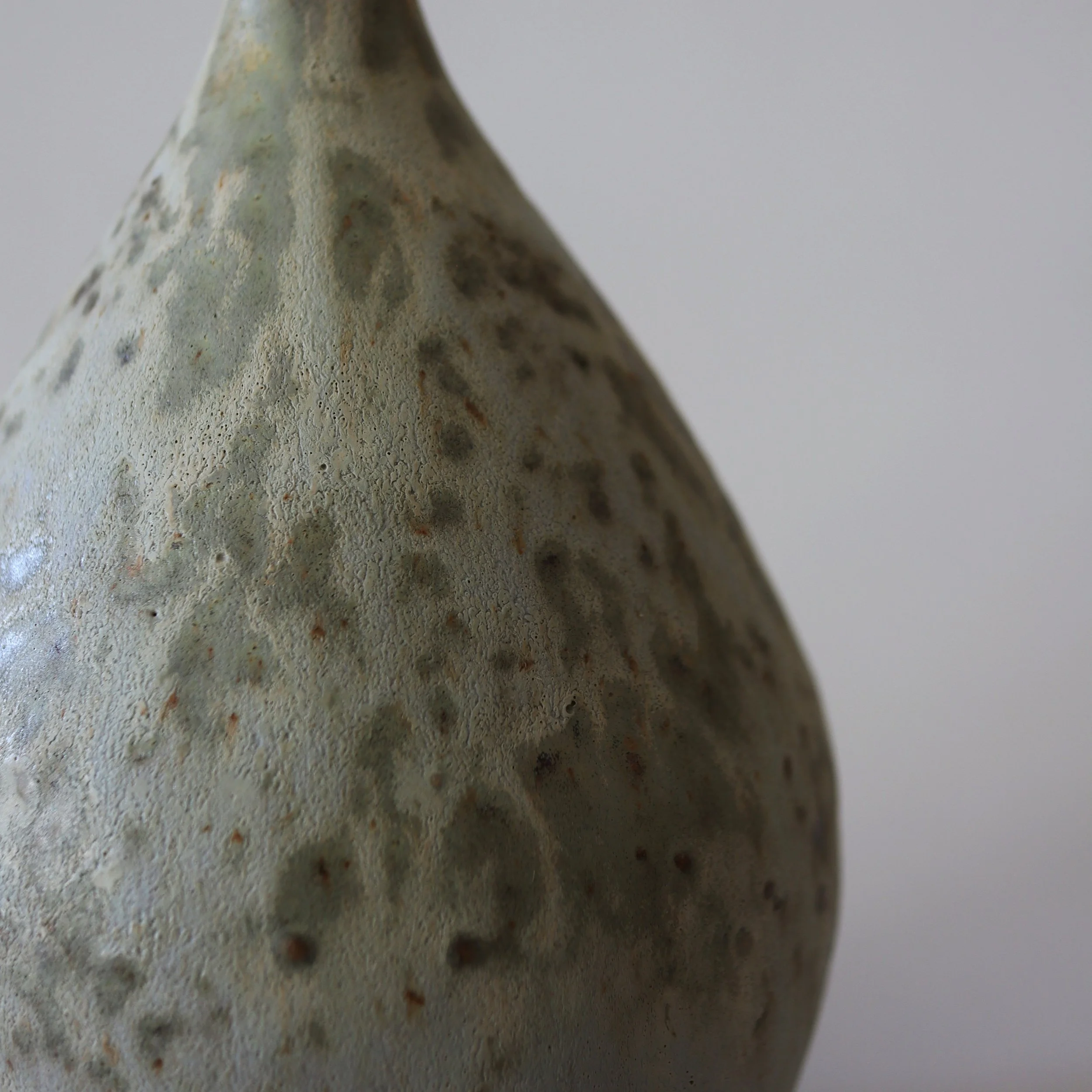 Close-up of a textured, speckled ceramic vase with a narrow neck and rounded body against a plain background.