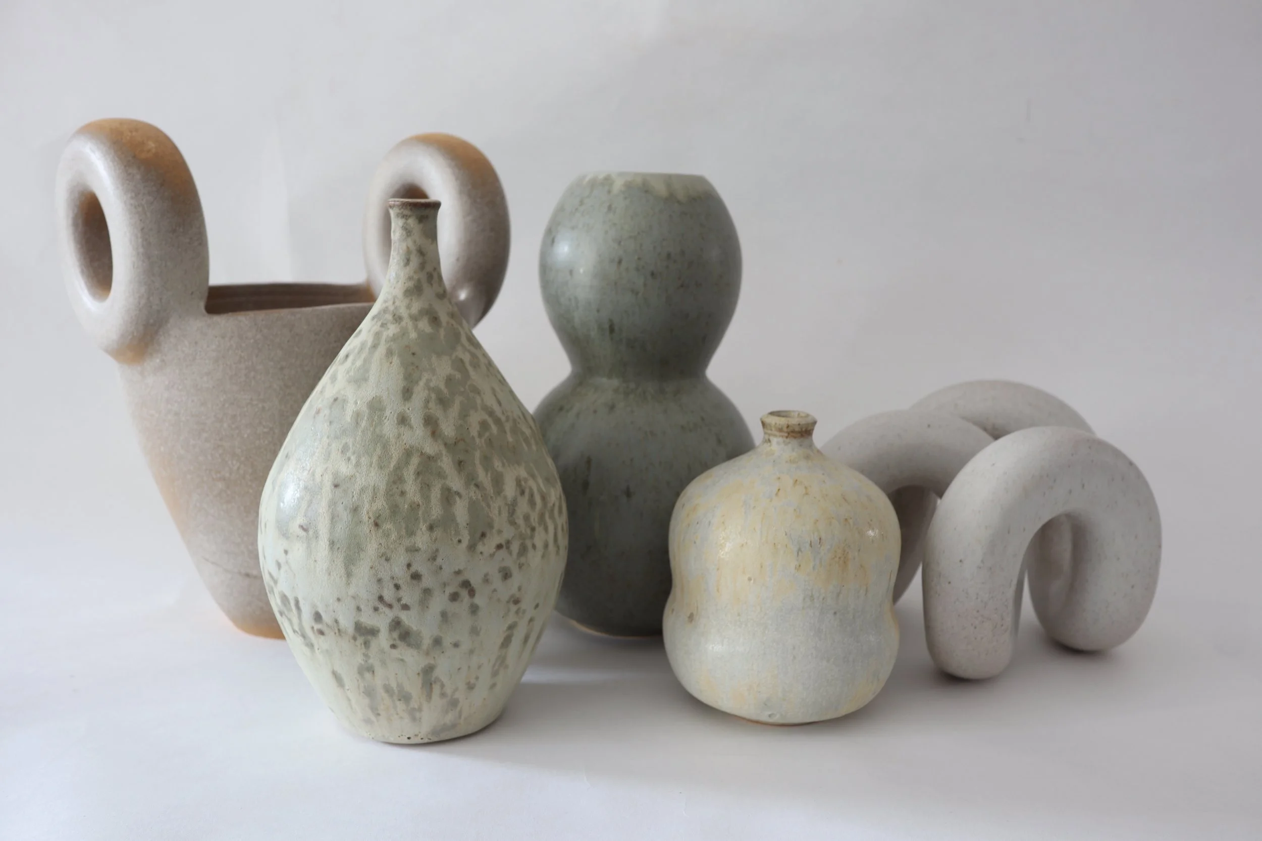 Collection of six ceramic vases and pots with varying textures and shapes on a white surface against a light background.