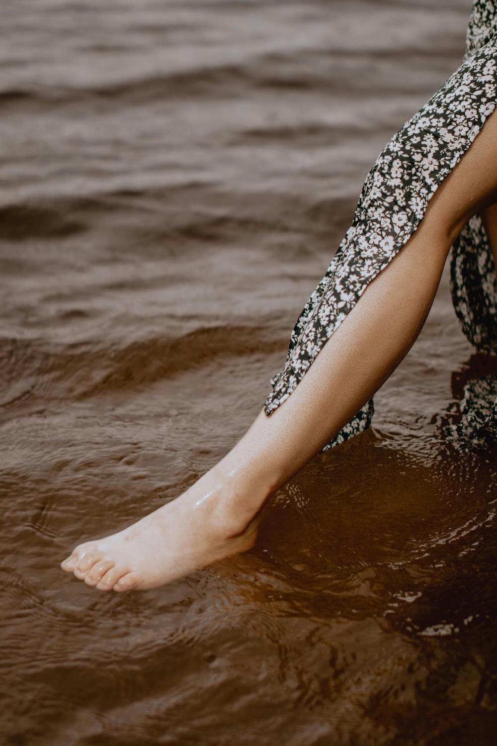 Close-up of a person with a floral dress dipping their leg in water.