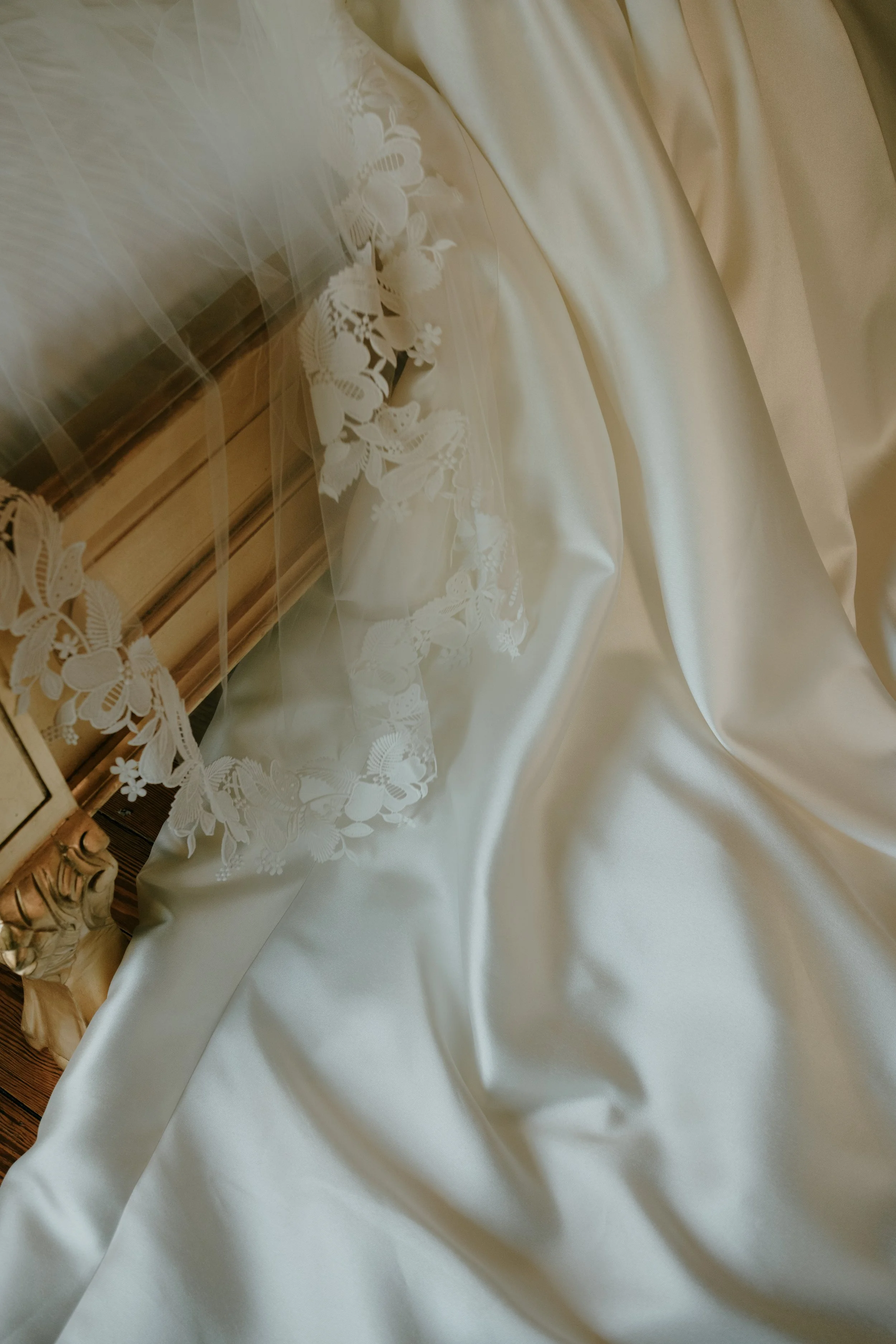 Un drap de satin blanc avec des broderies florales, posé sur un meuble en bois avec une sculpture décorative.