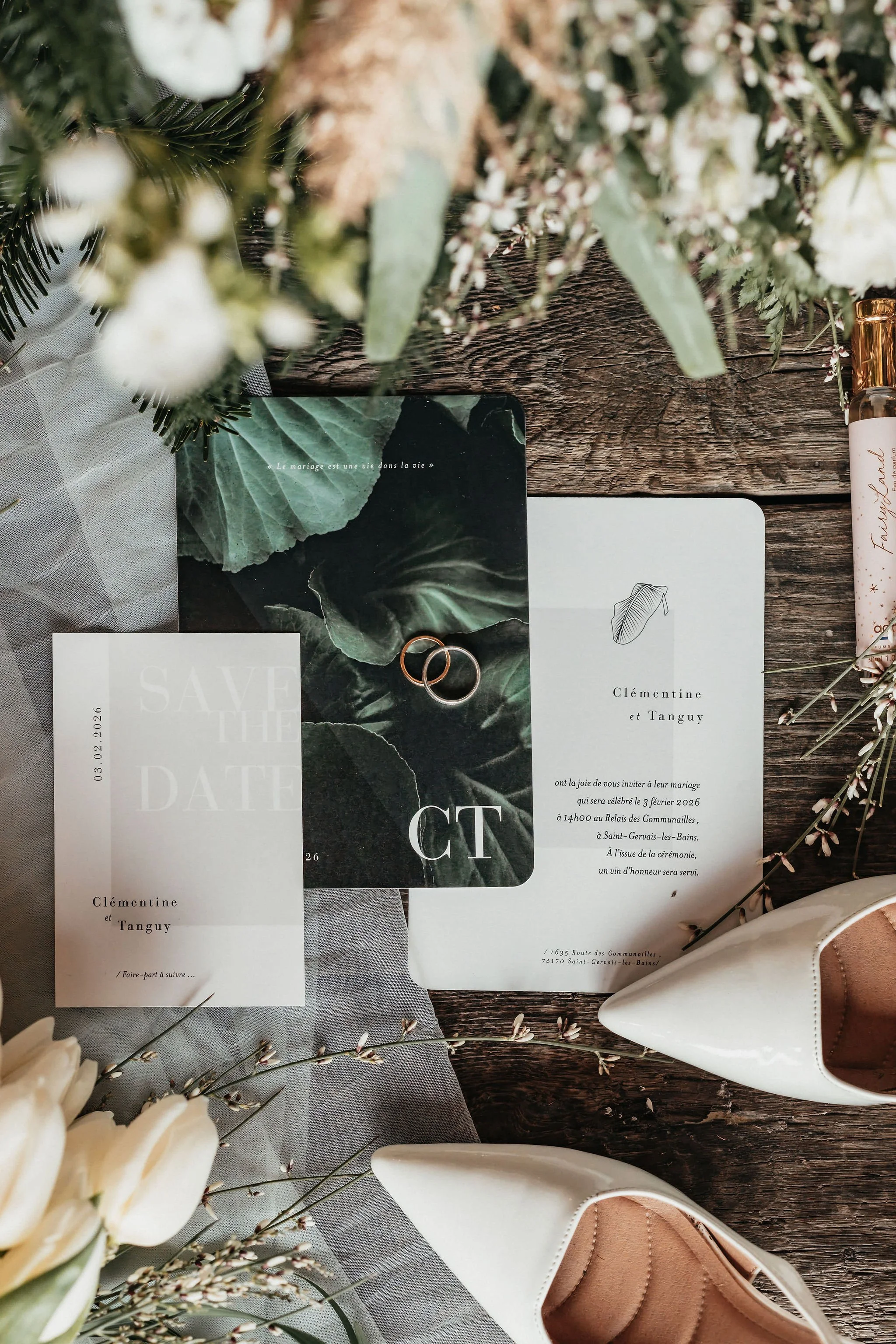 Invitation de mariage, alliance, et accessoires de mariage avec fleurs et chaussures blanches vintage sur une table en bois.