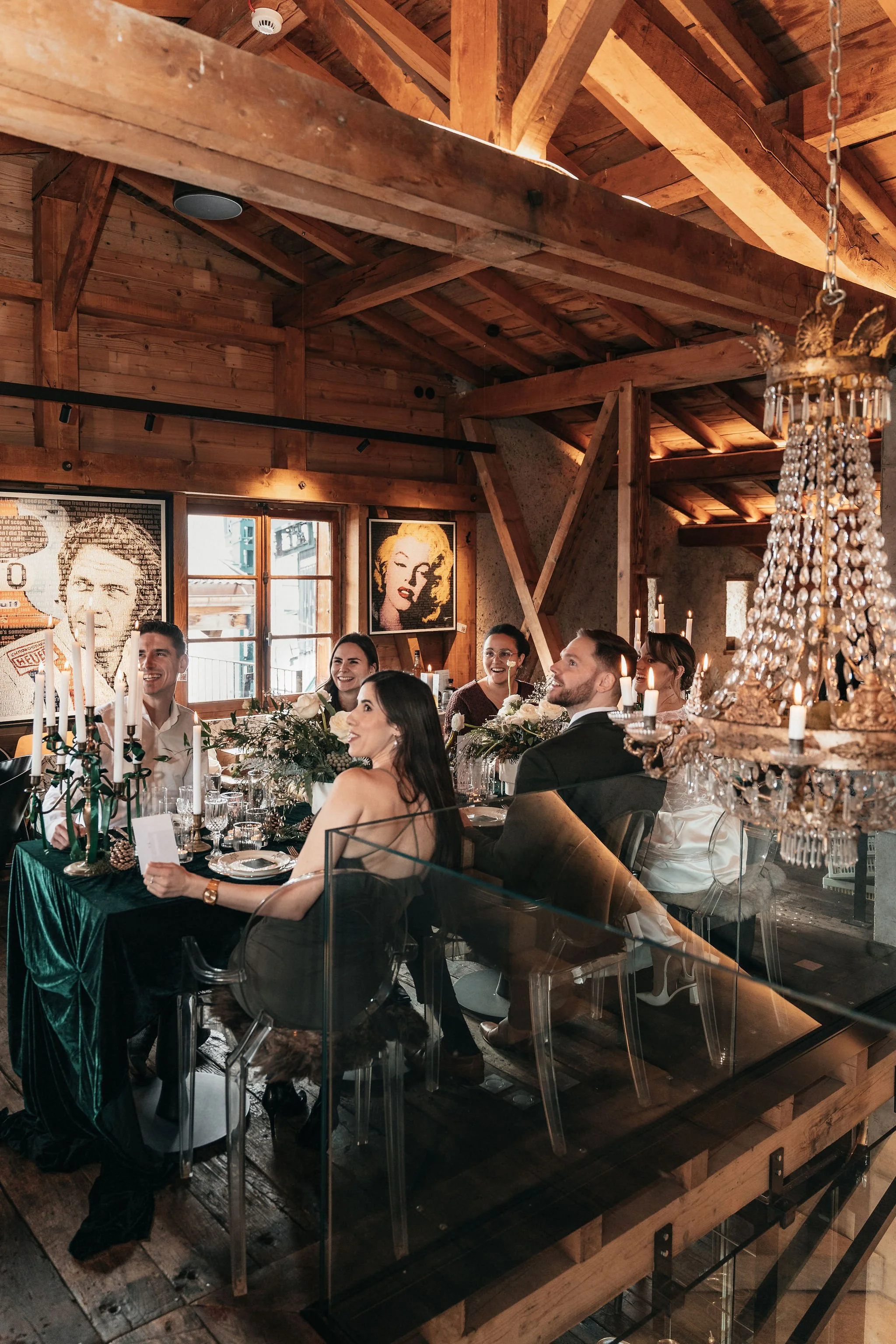 Groupe de personnes assises autour d'une table lors d'un dîner dans un espace décoré avec des œuvres d'art célèbres et un lustre chandelier chandelier, dans une ambiance chaleureuse avec beaucoup de bois.