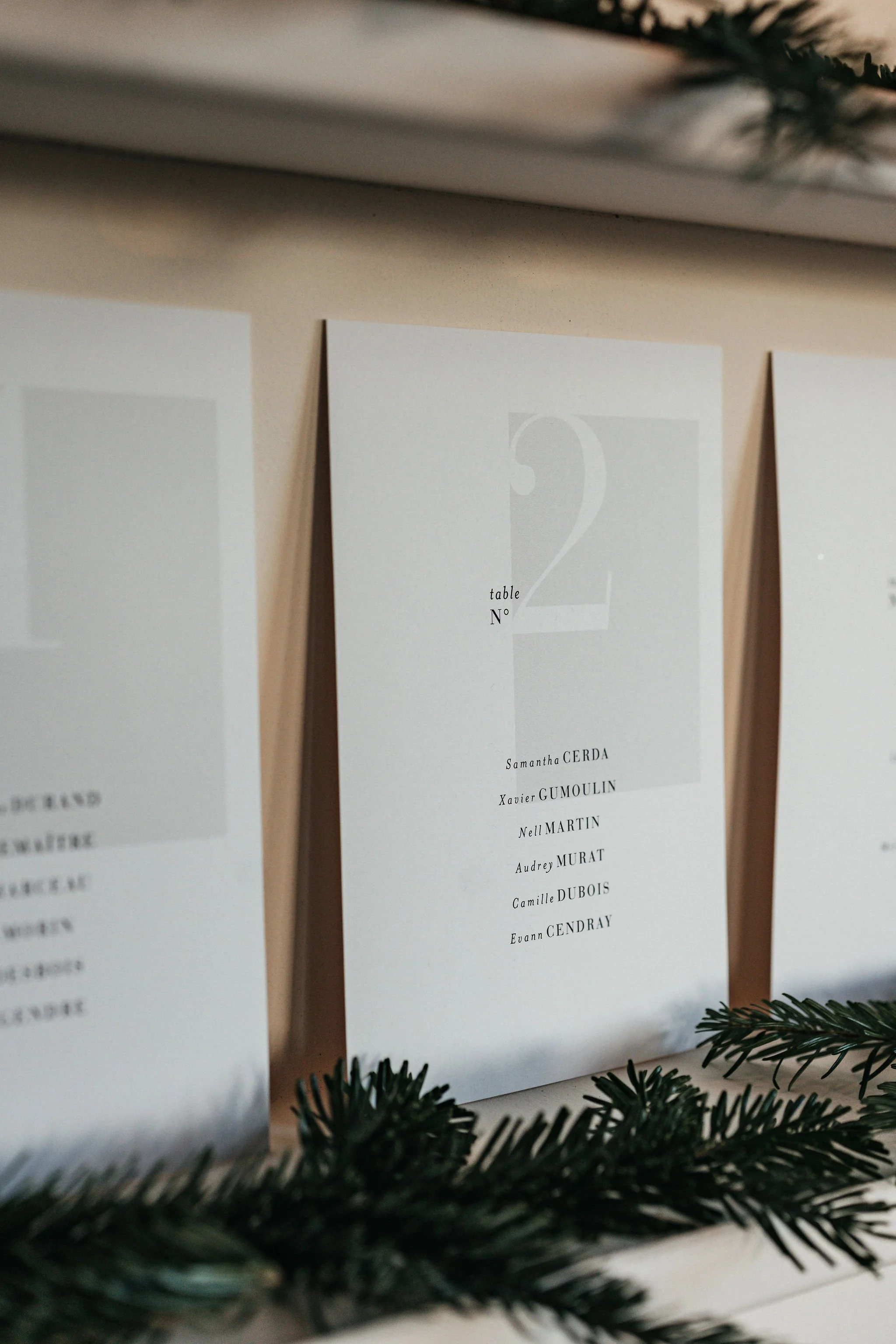 Menu de table pour un événement, affichant le numéro de la table 2, avec une liste de noms sous le titre. Décorations de Noël avec des branches de sapin en premier plan.