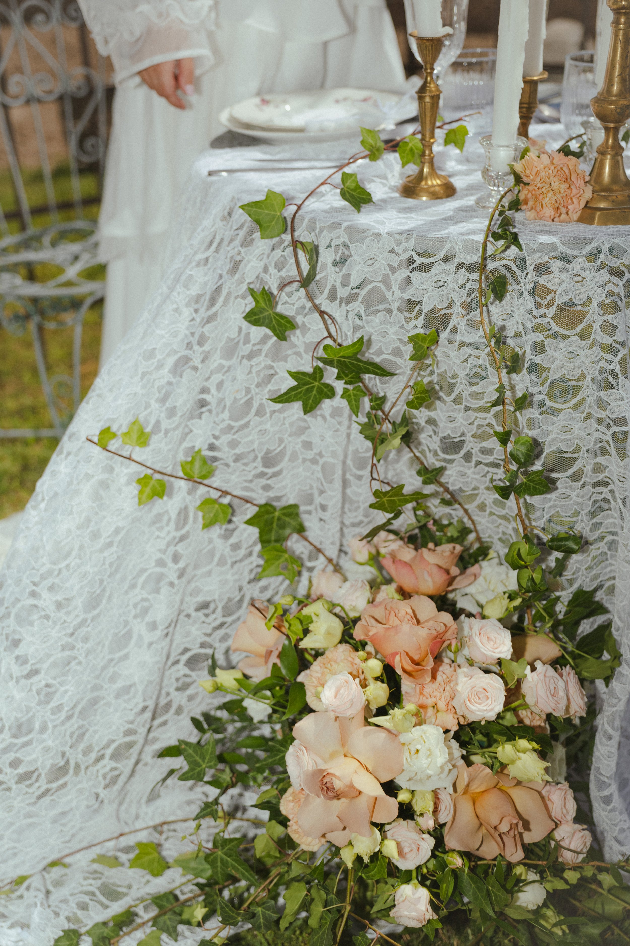 Une table de mariage décorée avec une nappe en dentelle blanche, des bougies dans des chandeliers dorés, des fleurs pastel et des branches de vigne verte.