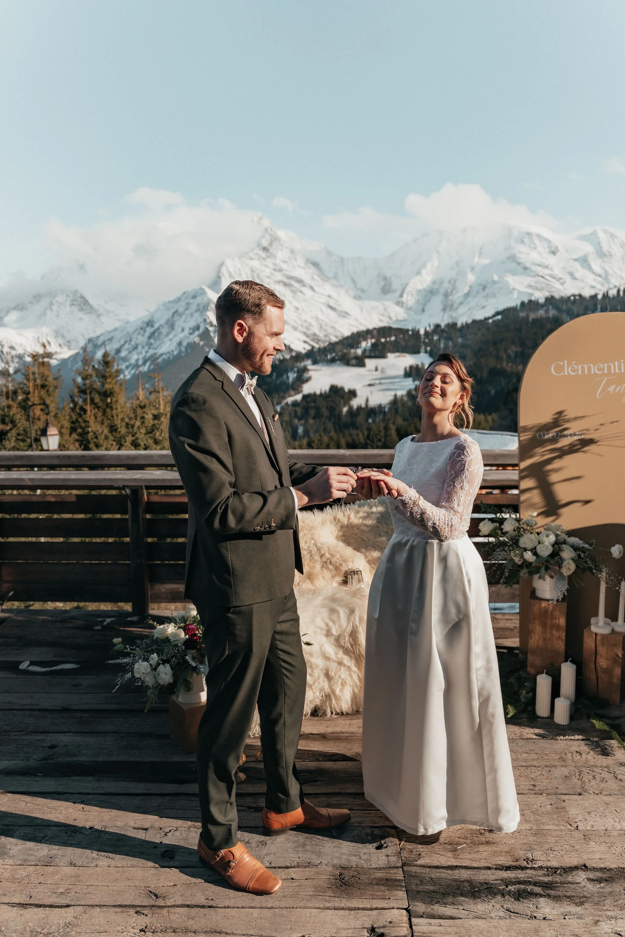 Un couple de mariés échange des alliances, avec des montagnes enneigées en arrière-plan lors d'un mariage en plein air.