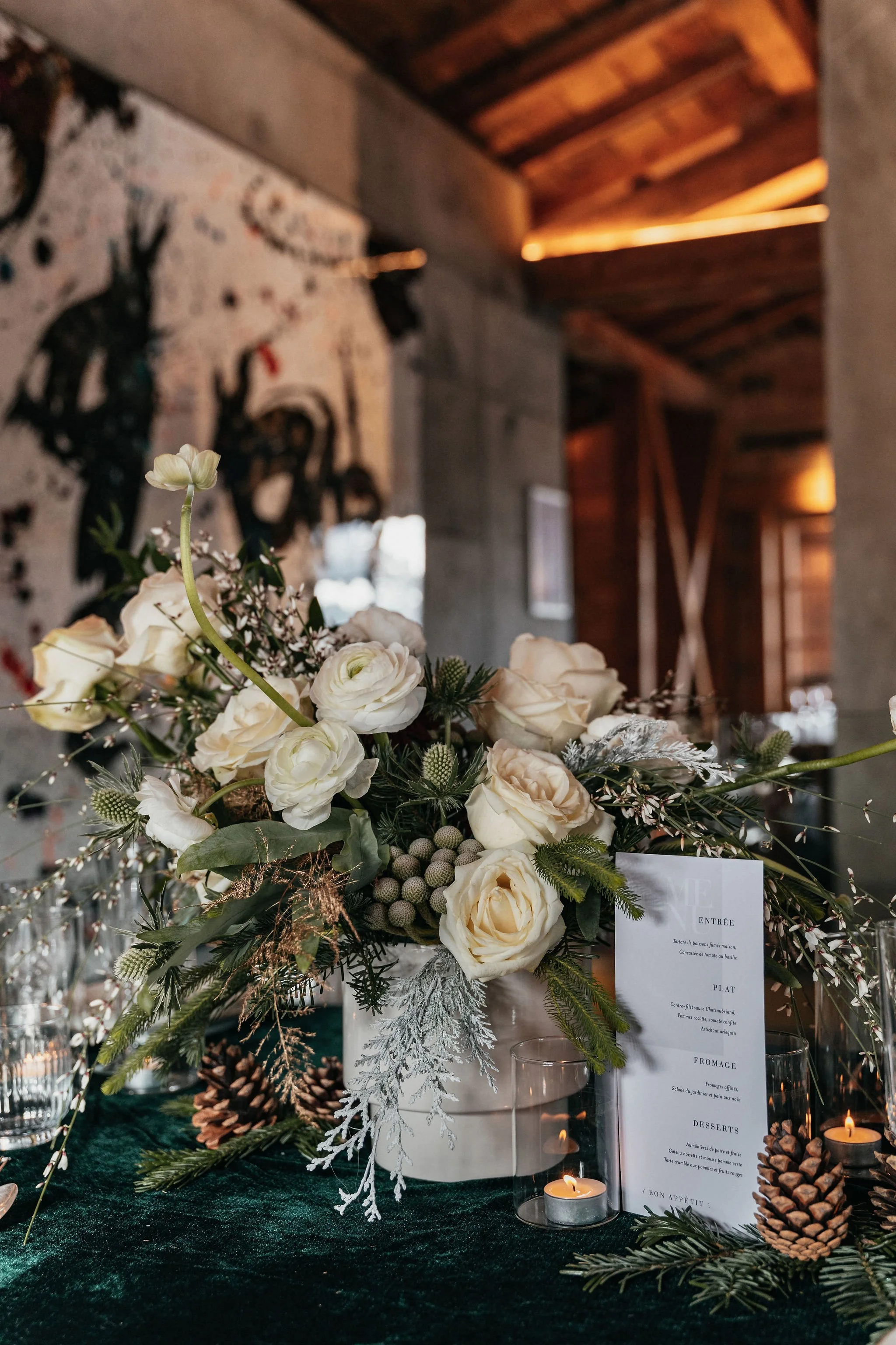 Arrangement floral blanc avec boules, pinecones, et bougies dans un décor intérieur rustique.