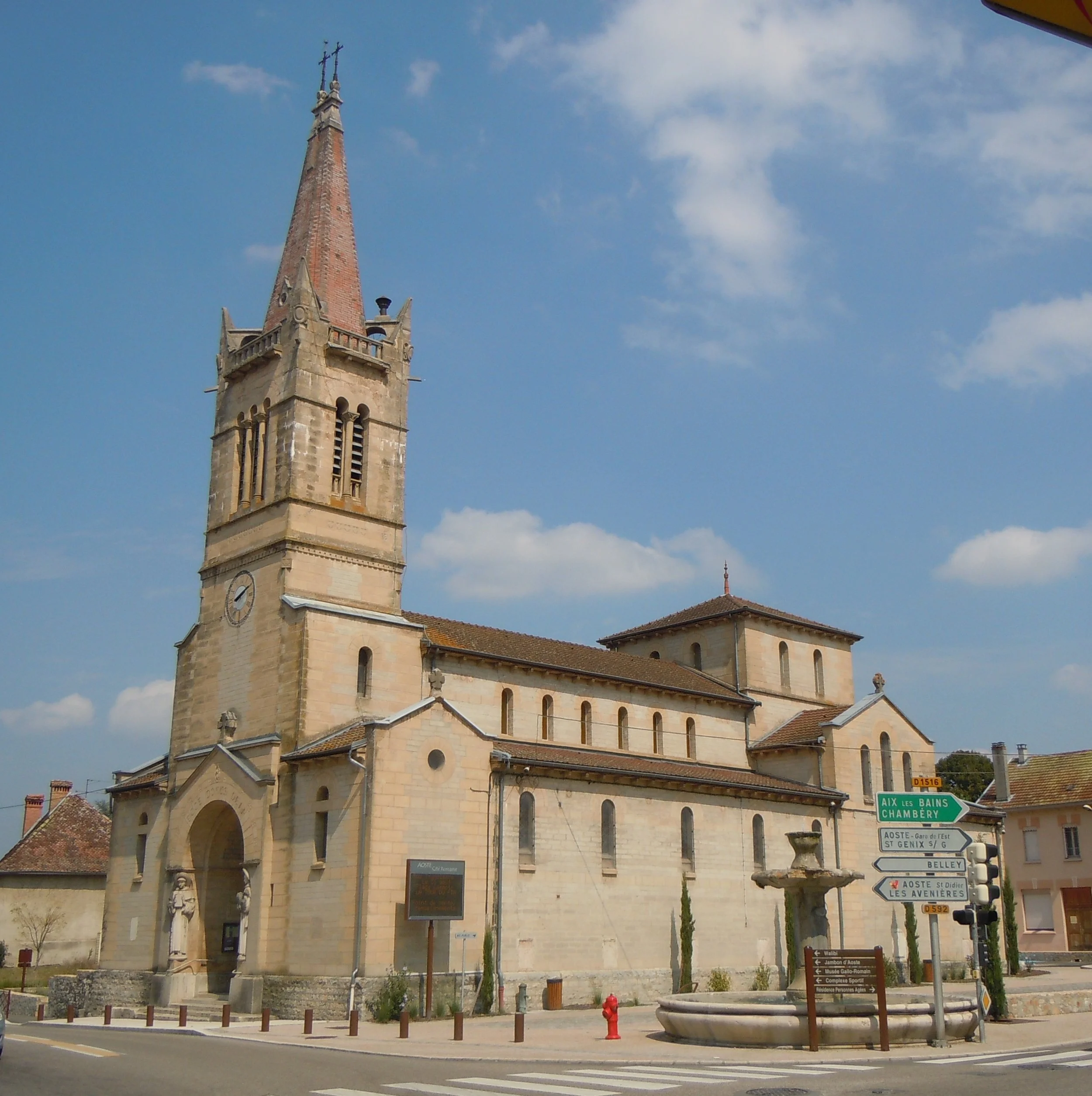 Une église en pierre avec une tour de clocher pointue et un horloge, située dans une ville en France, sous un ciel bleu avec quelques nuages.
