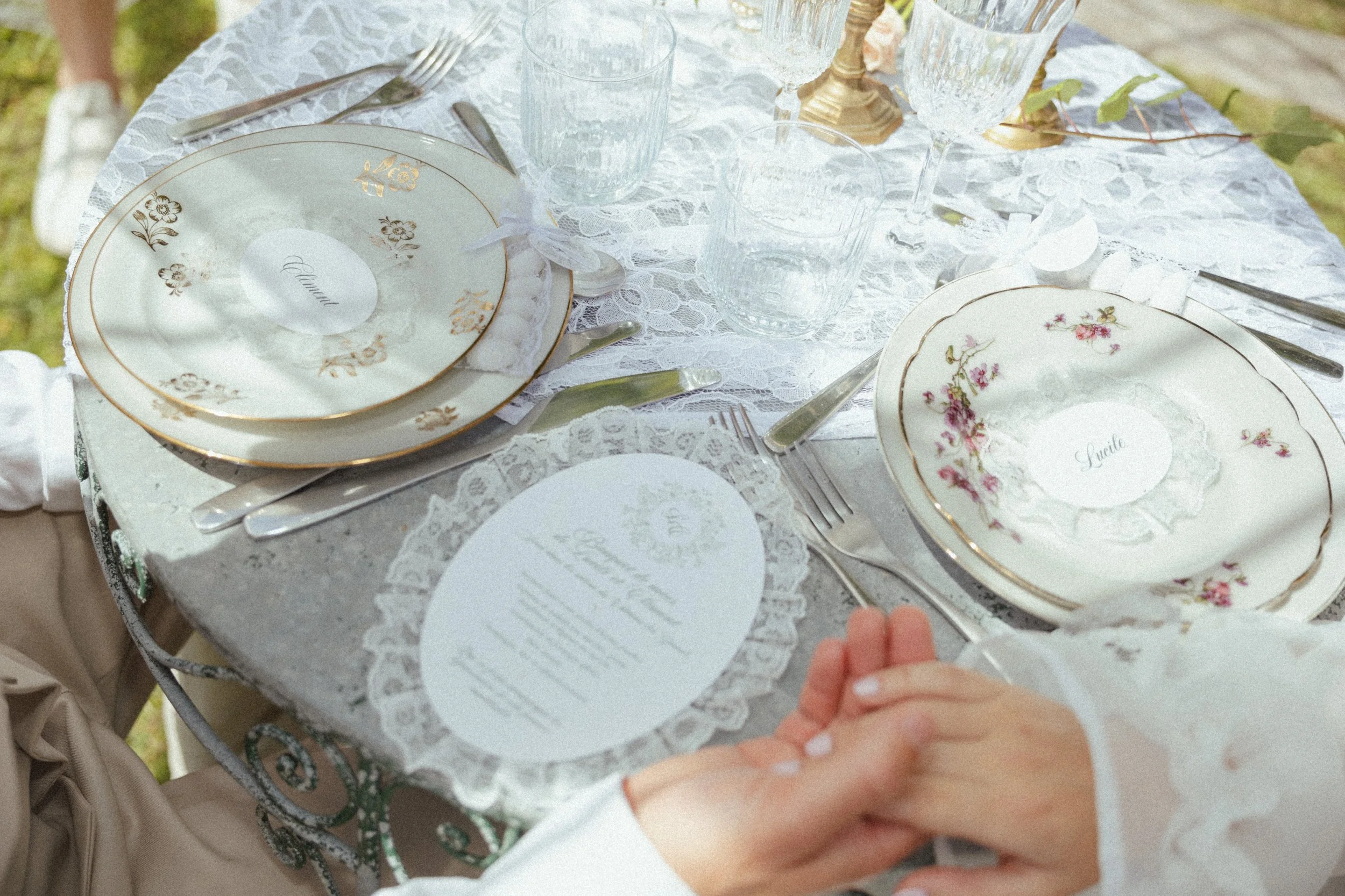 Une table de fête ornée en blanc avec des assiettes en porcelaine à motifs floraux, des verres en cristal, des couverts en argent, des bougies et des décorations naturelles, prête pour un repas élégant.