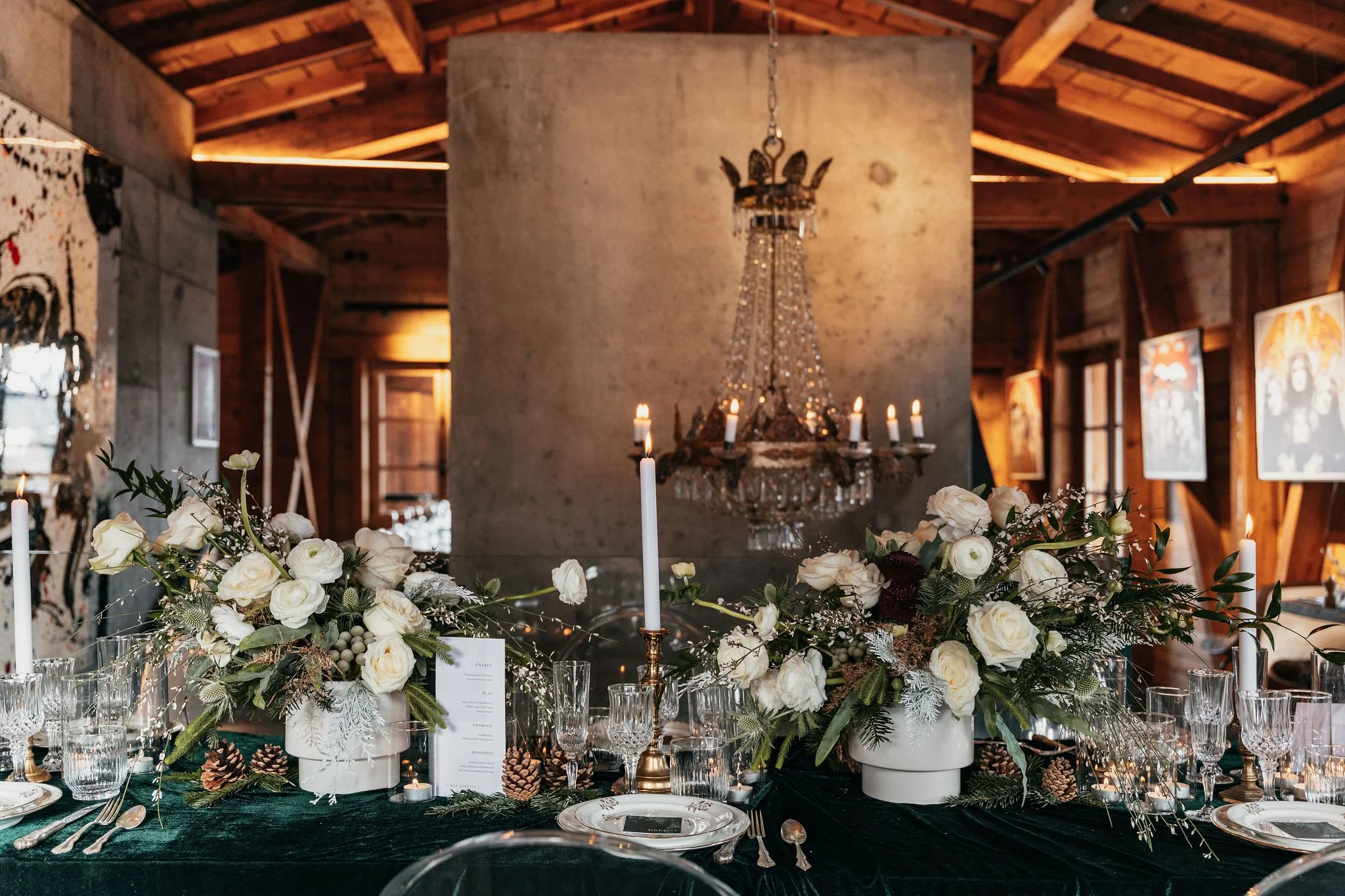 Table décorée avec des fleurs blanches, bougies et cristaux, dans un intérieur en bois avec un chandelier suspendu en arrière-plan.