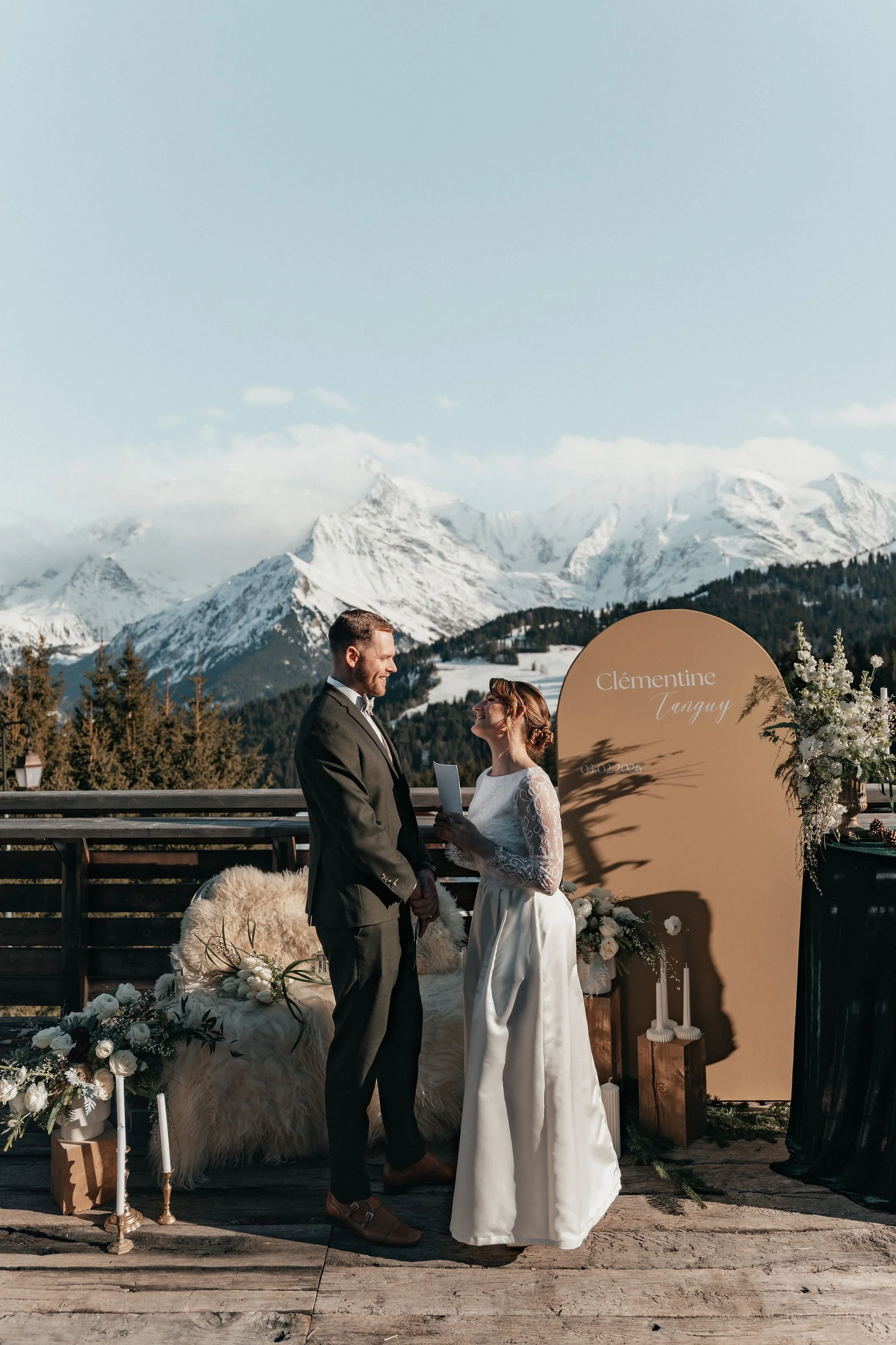 Un couple en mariage échange leurs vœux lors d'une cérémonie en plein air avec des montagnes enneigées en arrière-plan.