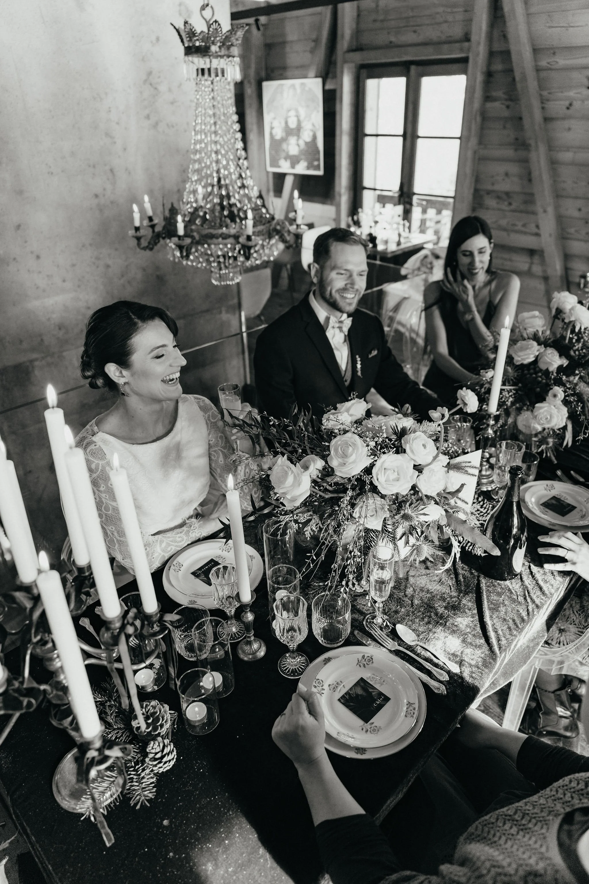 Groupe de personnes assises à une table lors d'une célébration, avec décorations florales et chandelles, dans une ambiance chaleureuse.