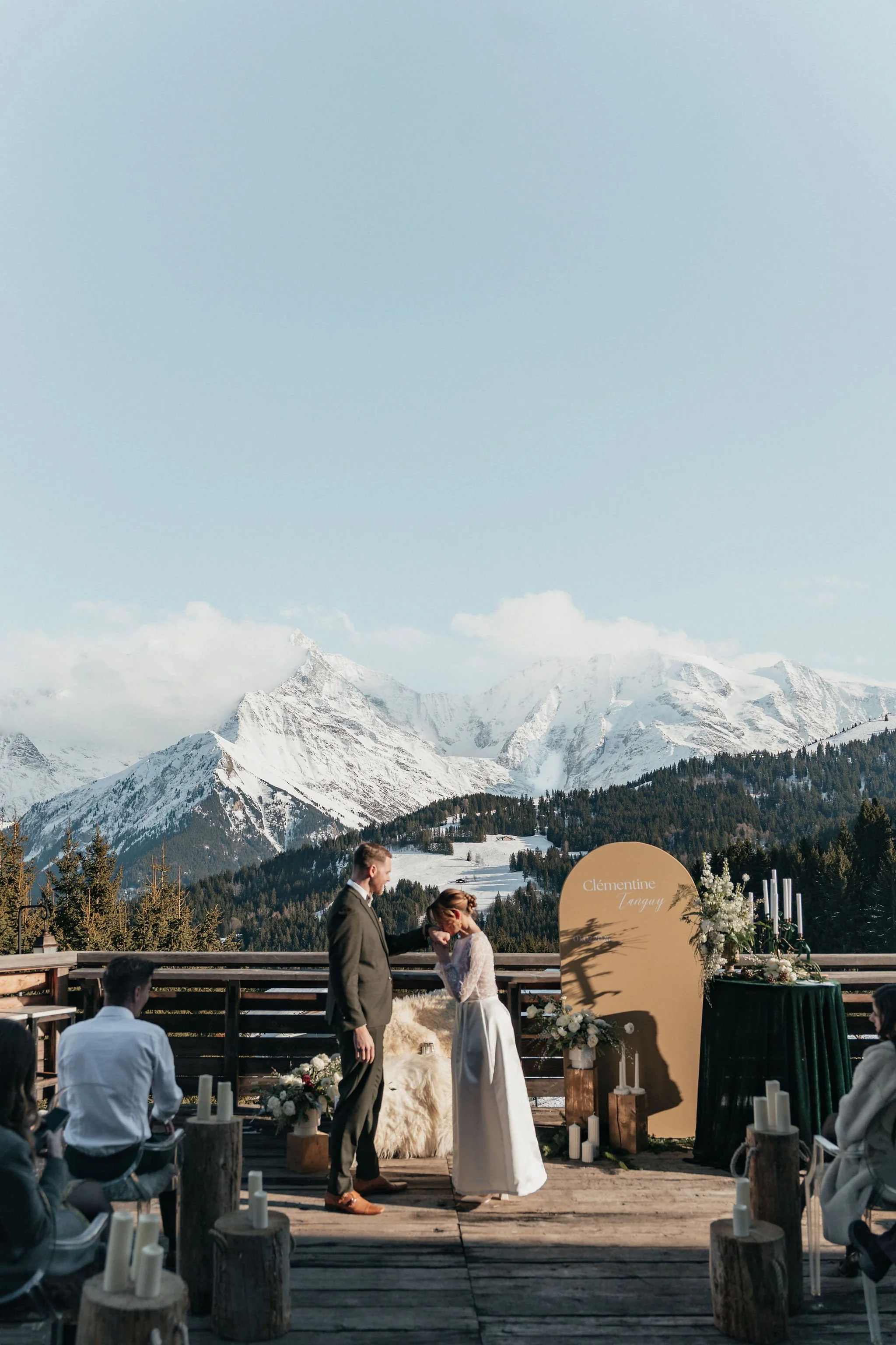 Un couple marié lors d'une cérémonie en plein air avec des montagnes enneigées en arrière-plan, décorée avec des fleurs et des bougies.