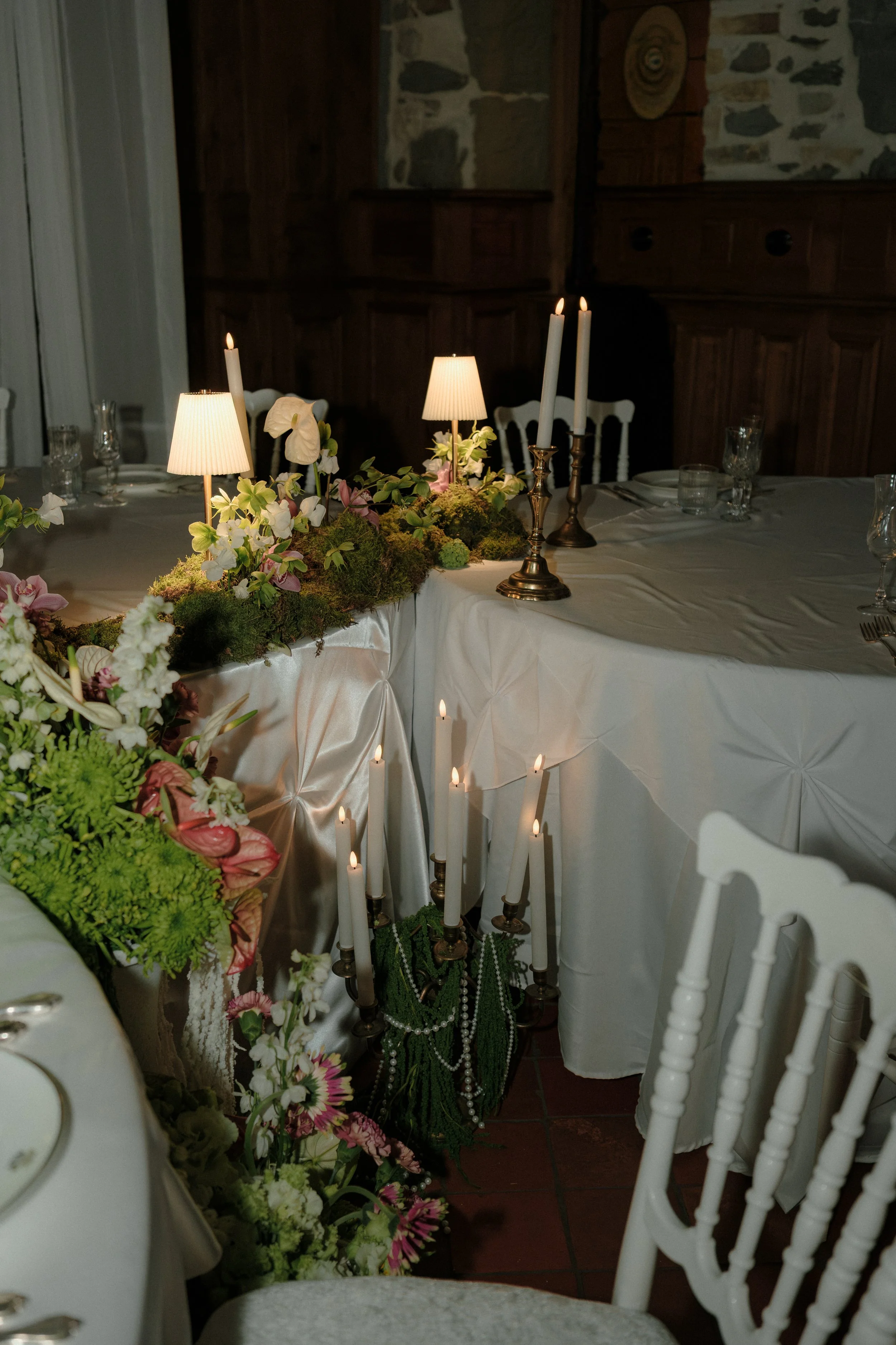 Langue d'une table de banquet décorée avec des lampes, des chandelles et des fleurs, dans un intérieur d'ambiance chaleureuse.