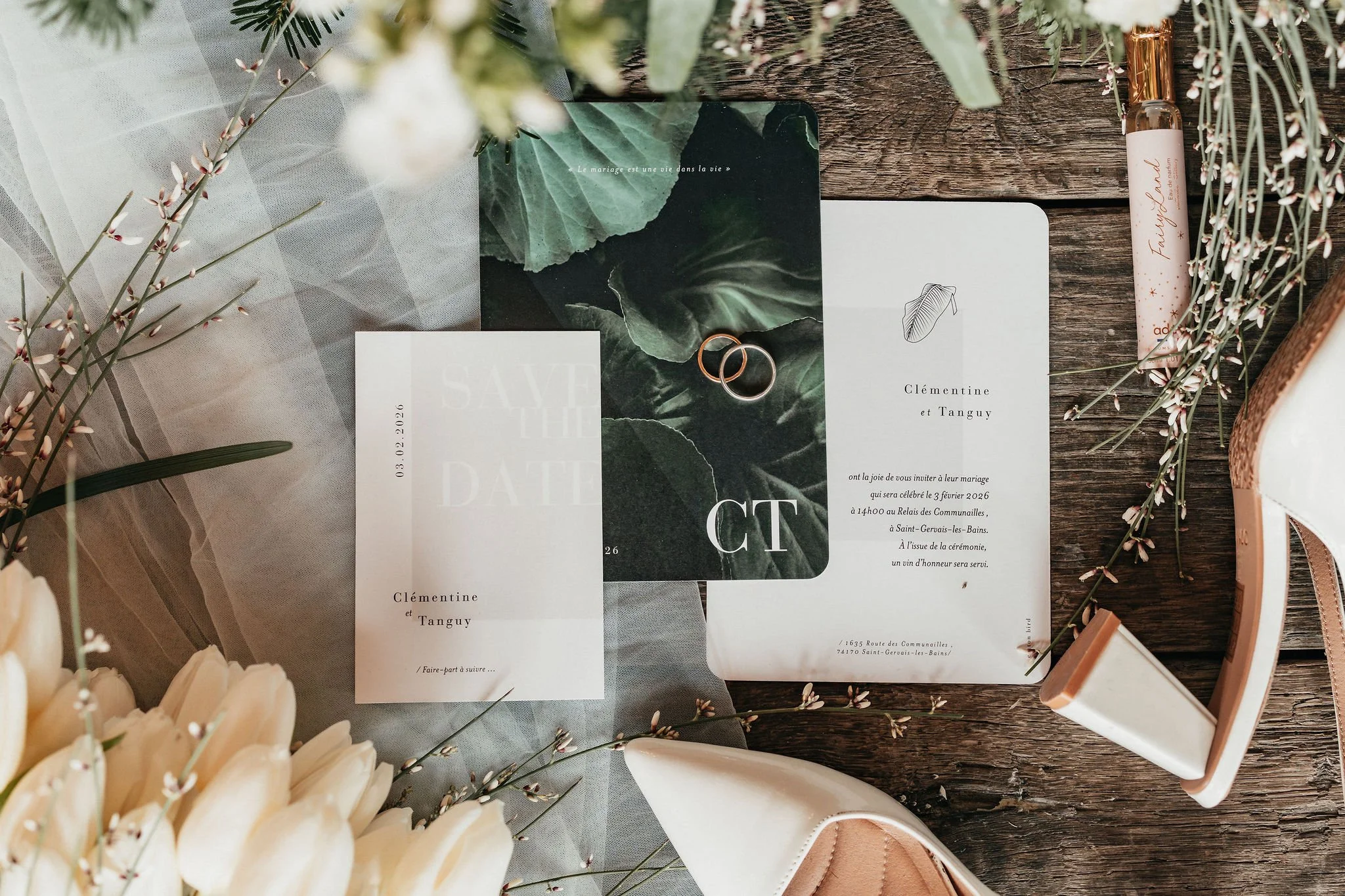 Invitation de mariage avec deux alliances, documents de mariage, fleurs et chaussures sur une surface en bois.
