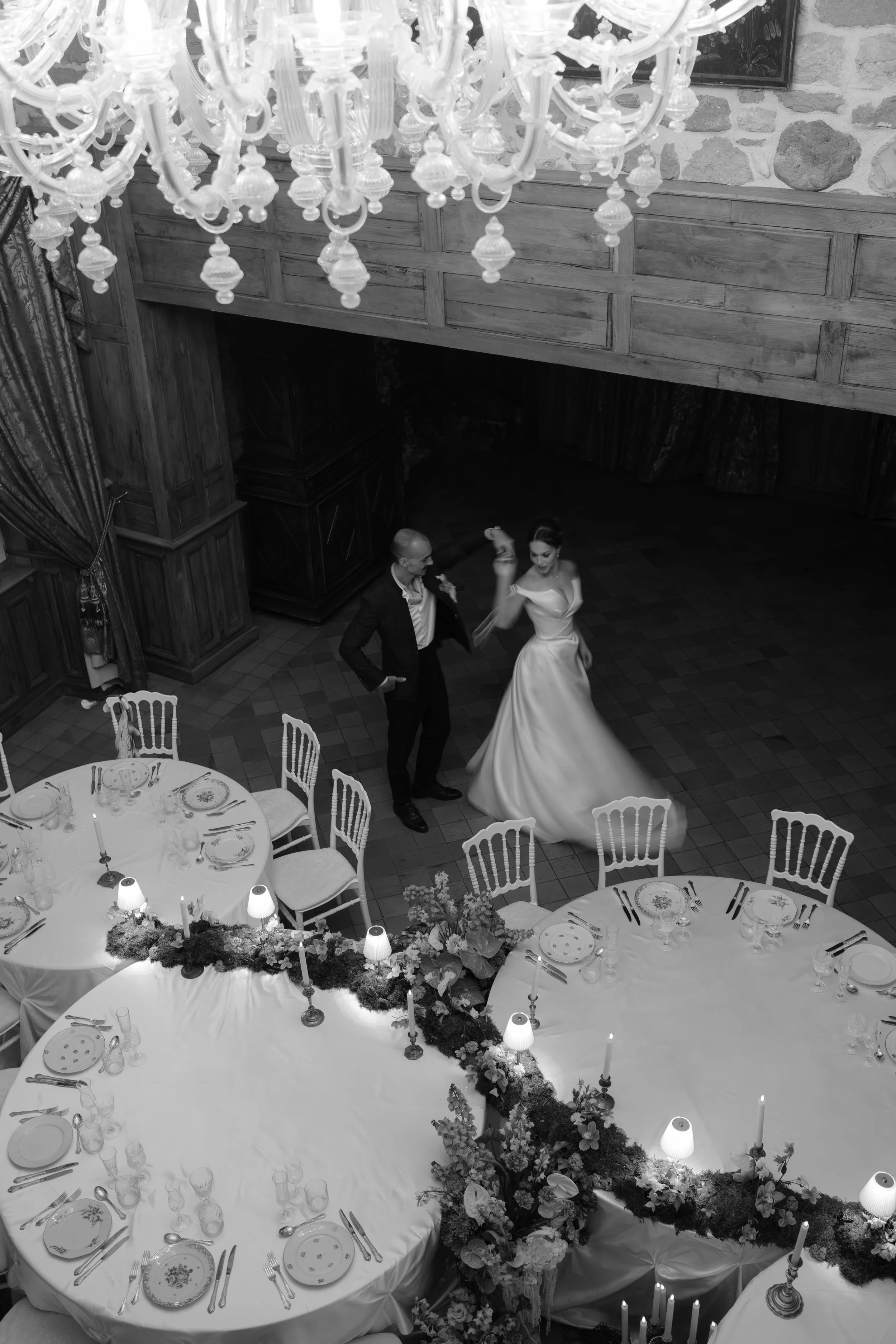 Deux personnes dansent lors d'une fête dans une salle élégante avec une table décorée et un chandelier au plafond.
