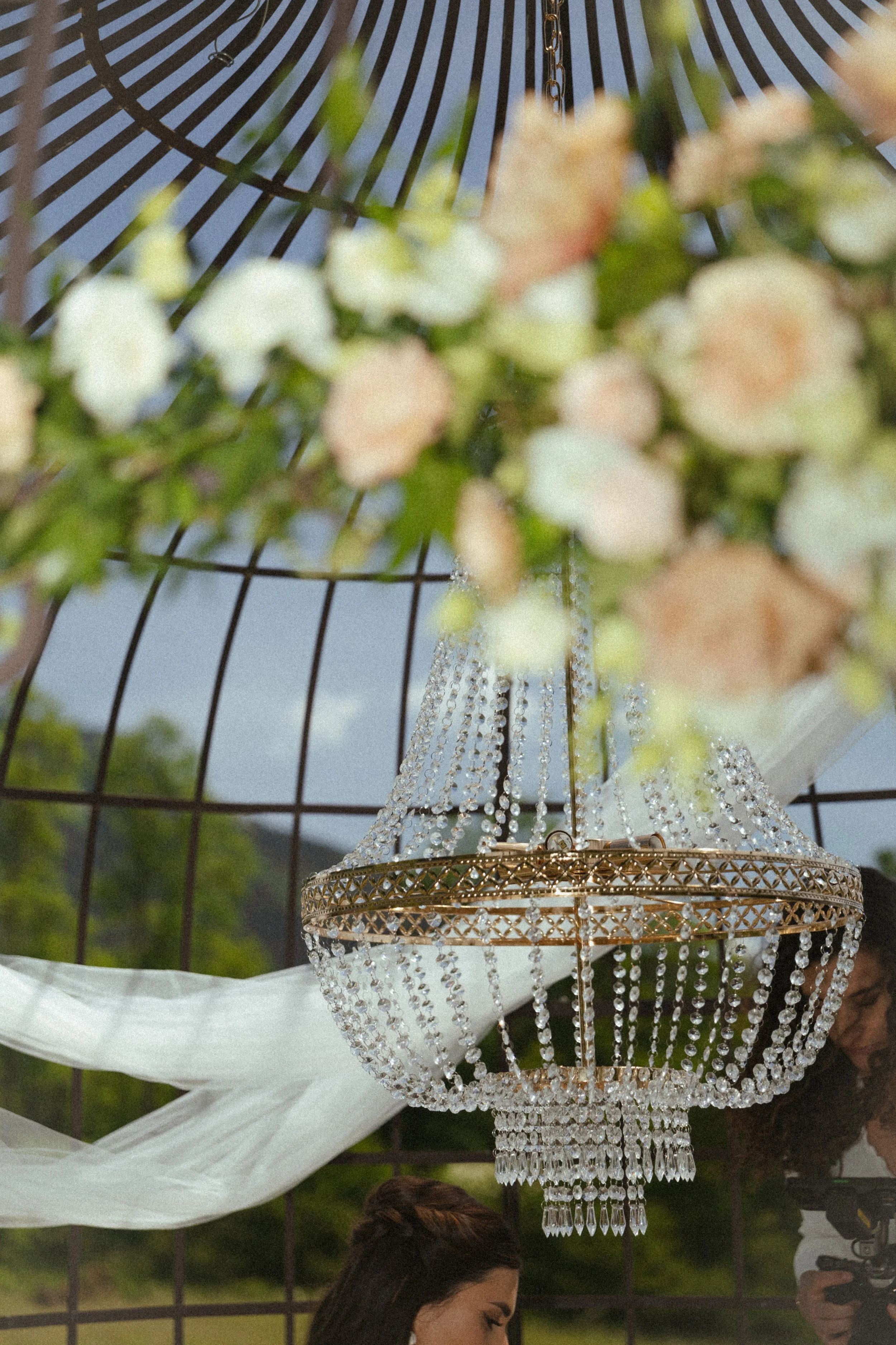 Une lanterne en cristal suspendue, avec des fleurs blanches et vertes en arrière-plan, et une personne en bas.