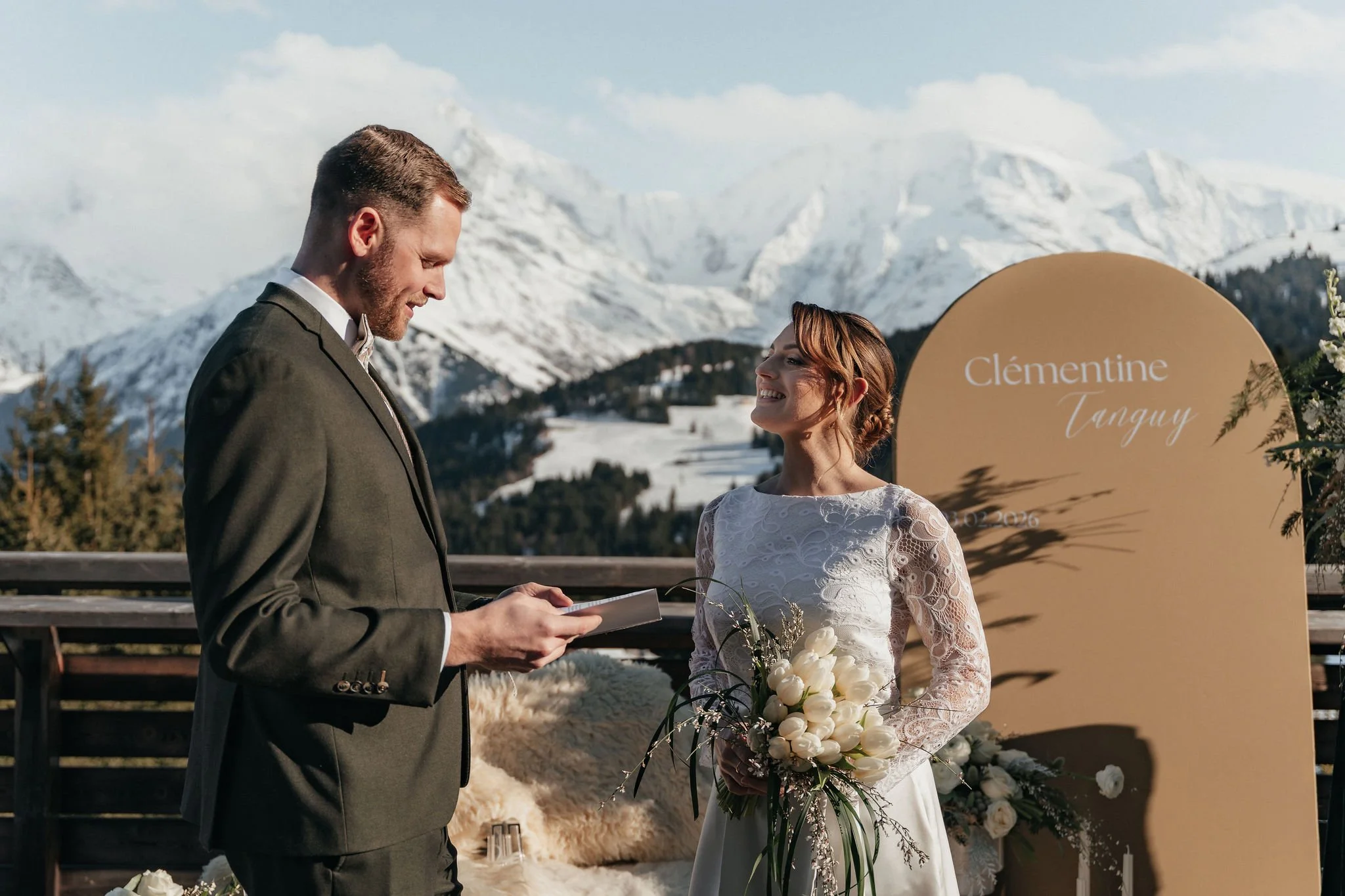 Un couple lors de leur mariage en montagne enneigée, le homme en costume et la femme en robe de mariée tenant un bouquet de fleurs blanches.