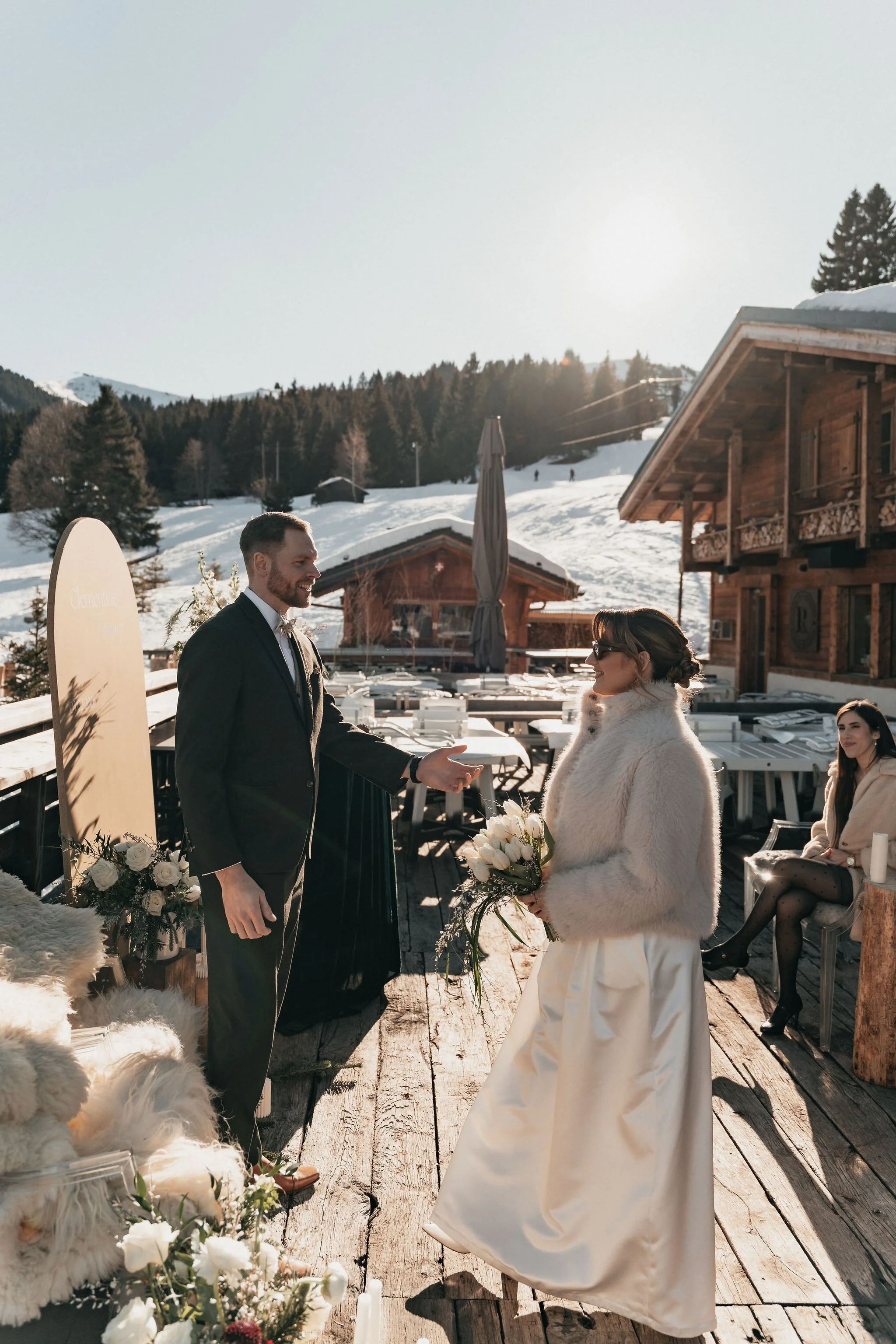 Un couple échange des vœux de mariage en extérieur dans un cadre montagnard enneigé, avec des amis assis à côté.