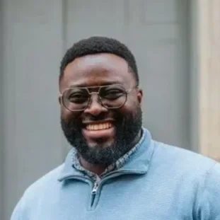 Portrait of a smiling man with glasses, a beard, and short hair, wearing a light blue jacket.