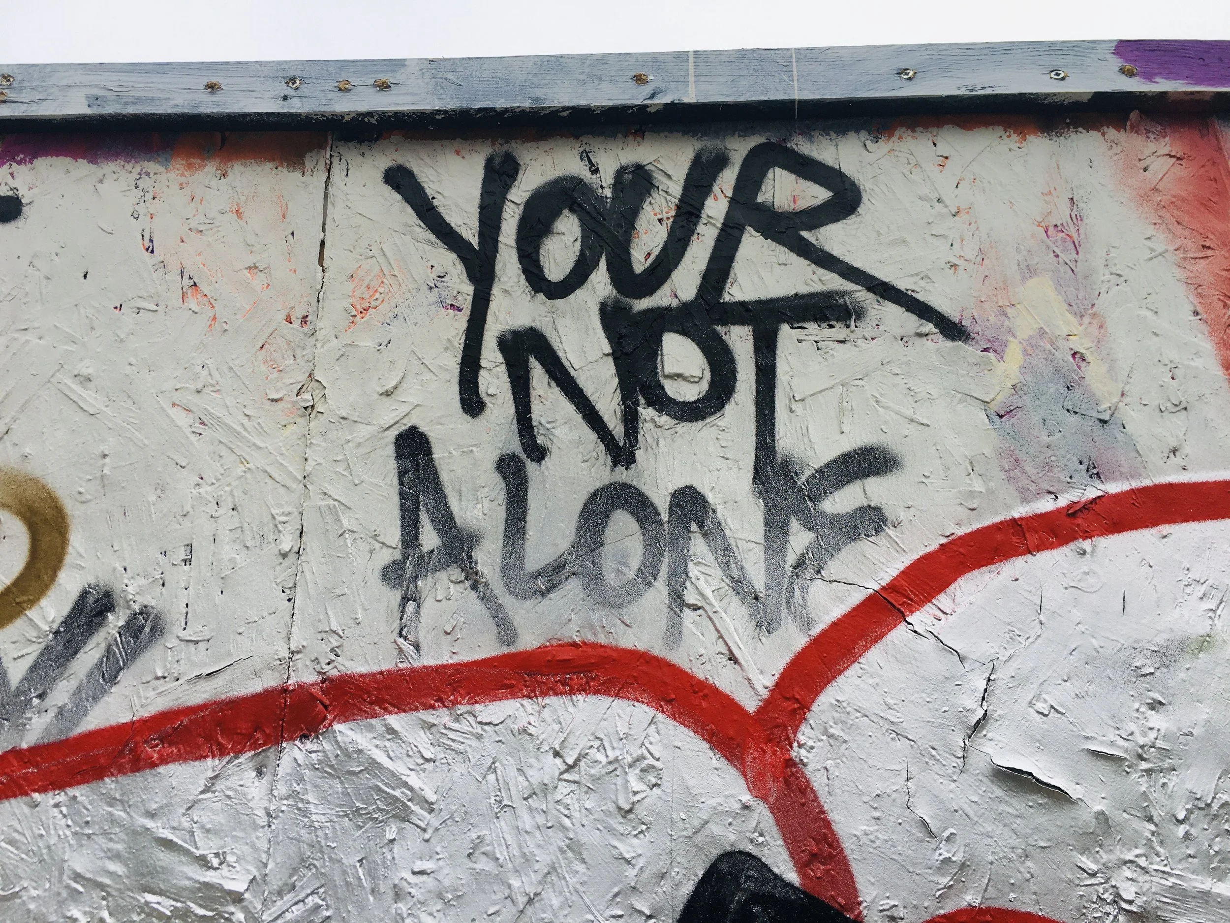 Graffiti on a wall with the message "You Are Not Alone" written in black spray paint.