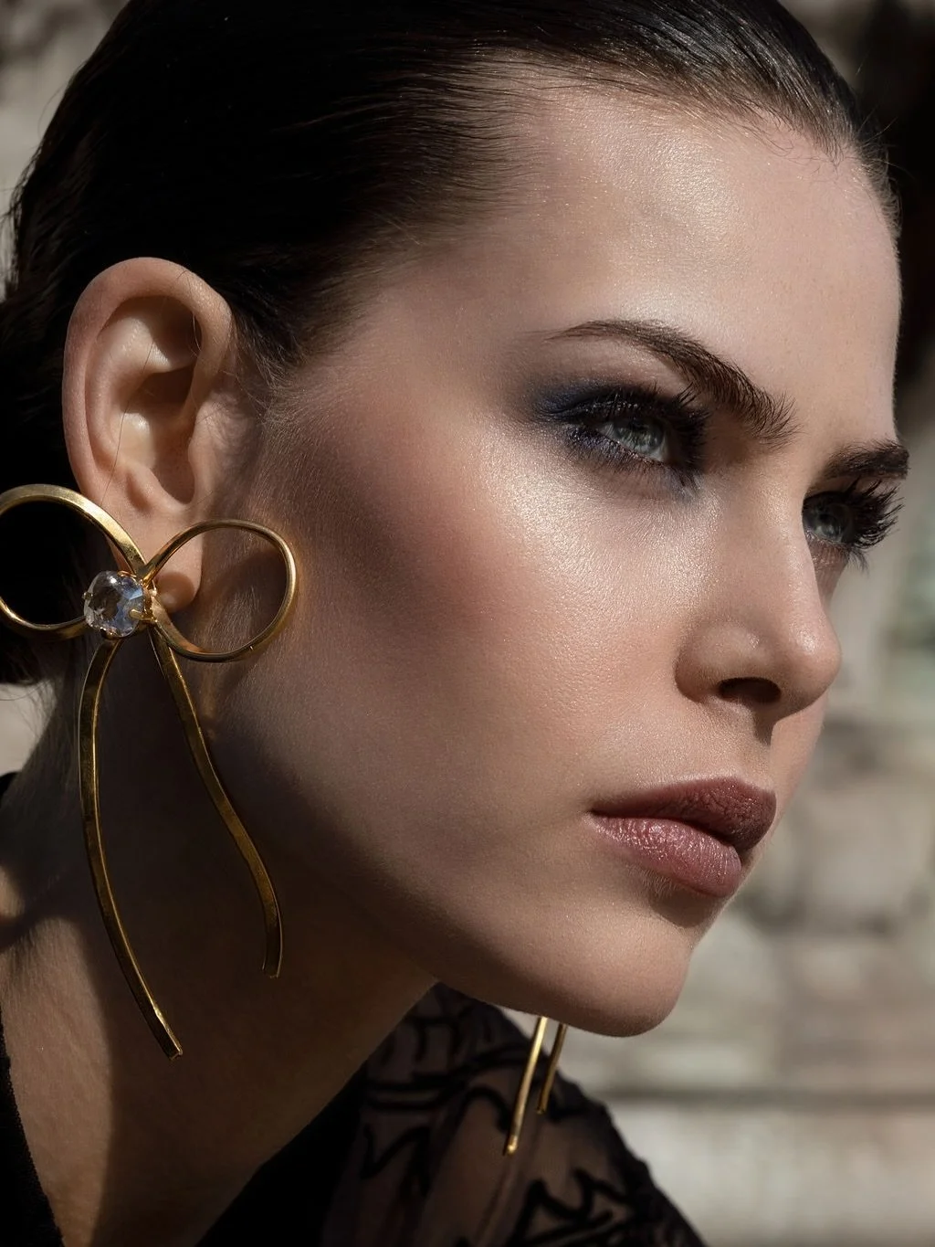 A close-up of a woman's face showing her makeup, hairstyle, and ornate gold earrings with a gemstone.