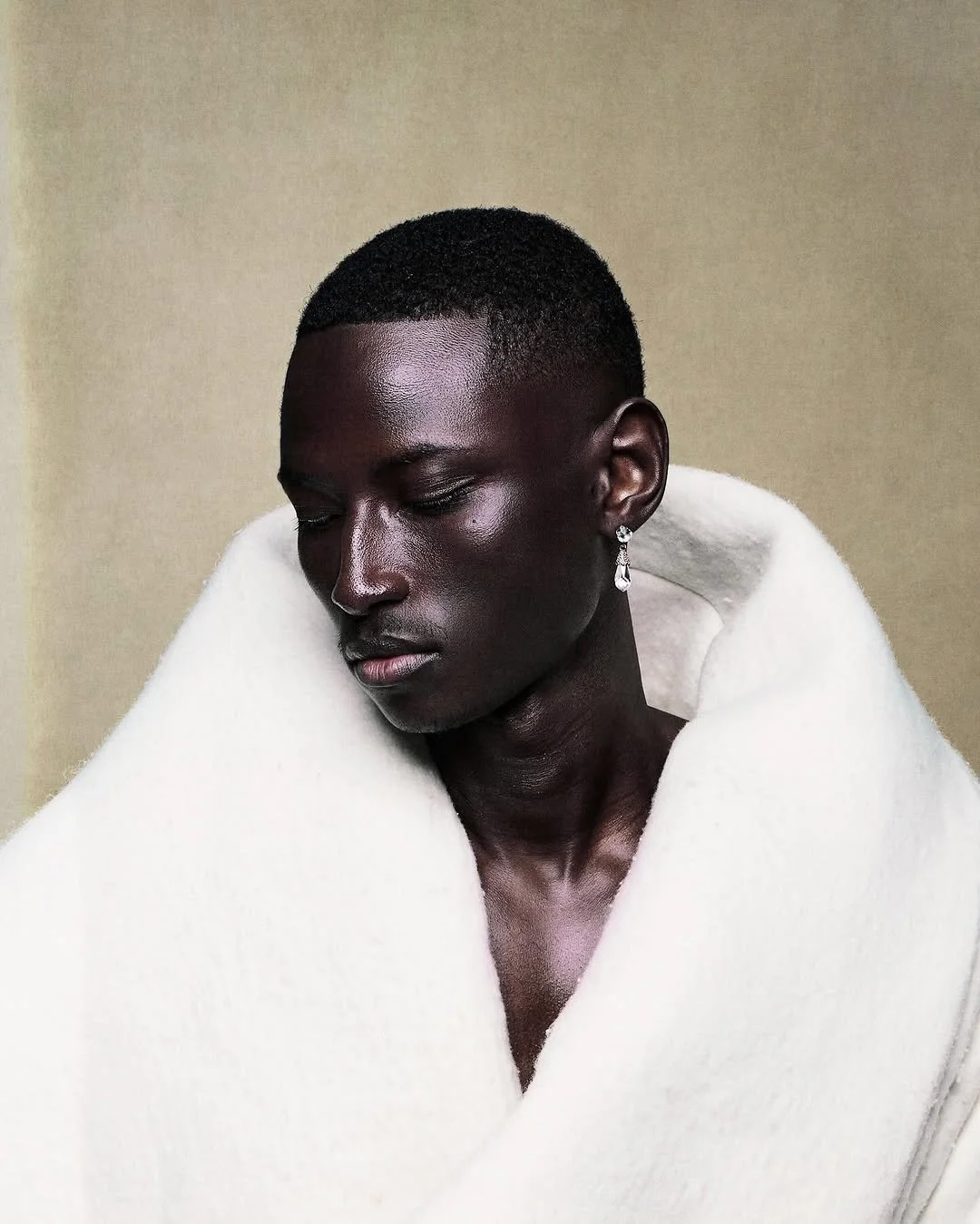 Portrait of a dark-skinned woman with short hair, wearing elegant earrings and wrapped in a white scarf against a plain background.