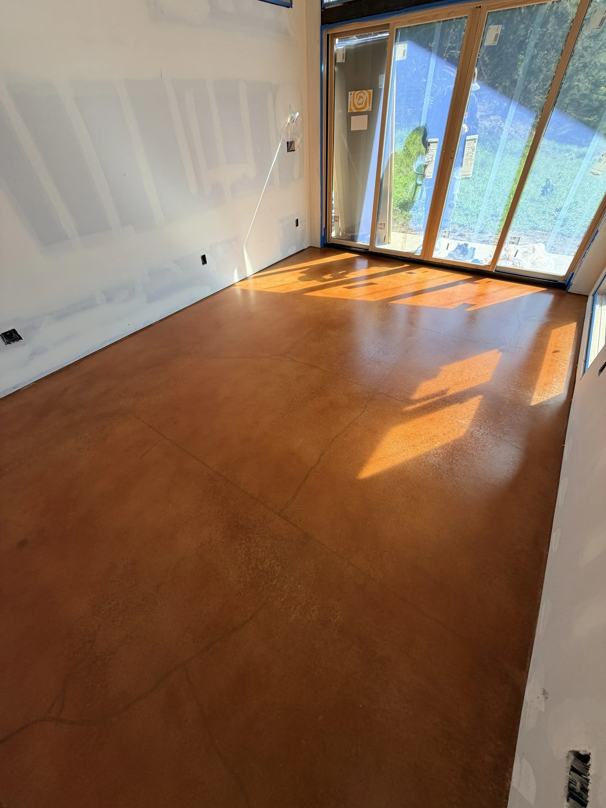 Room under construction with unfinished walls, electrical outlets, and a large sliding glass door leading to an outdoor area with trees and rocks. Concrete slab has a copper, orange, rustic, polished wax finish.