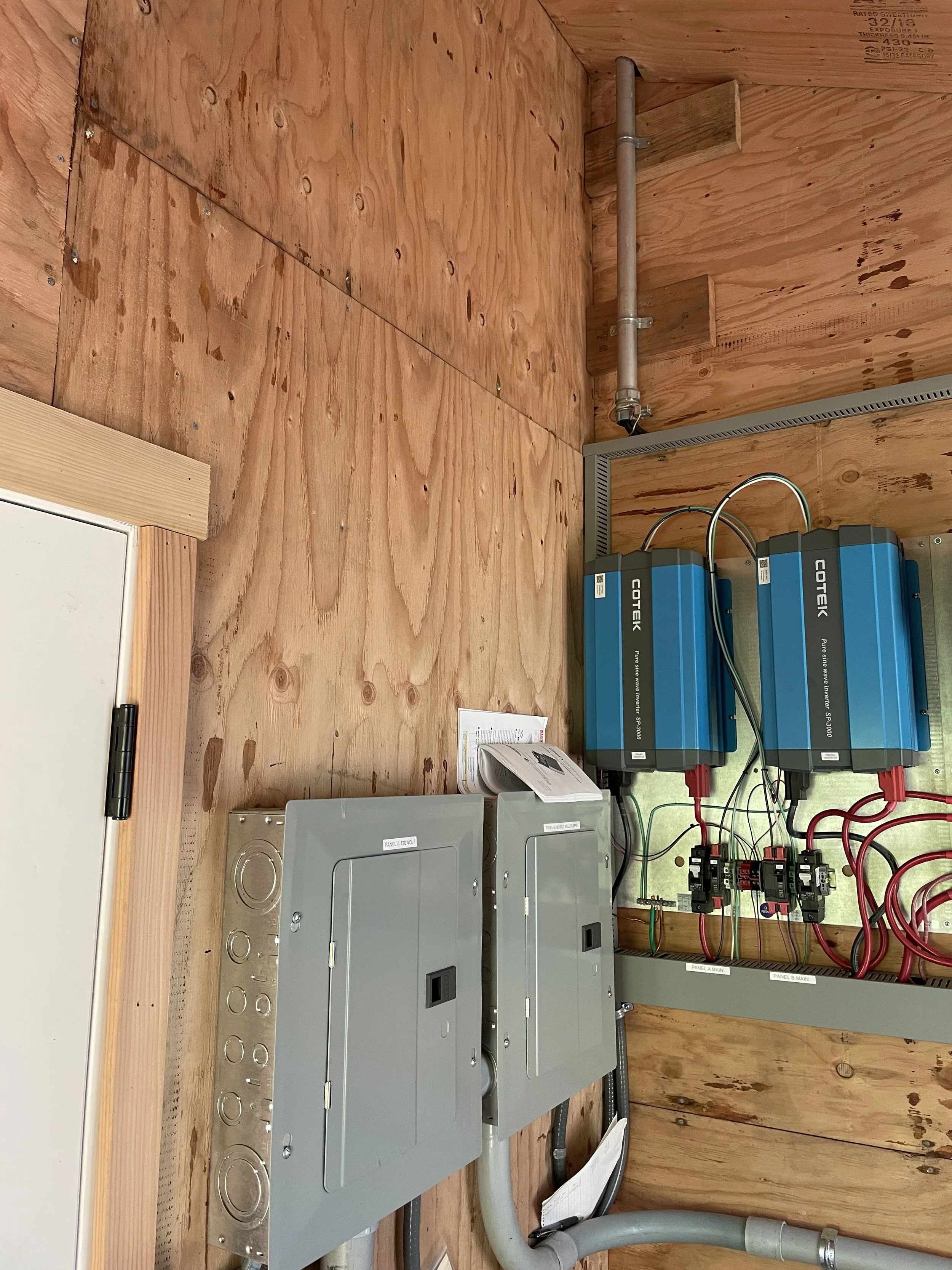 Electrical panels, wiring, and conduit inside a wooden enclosure.