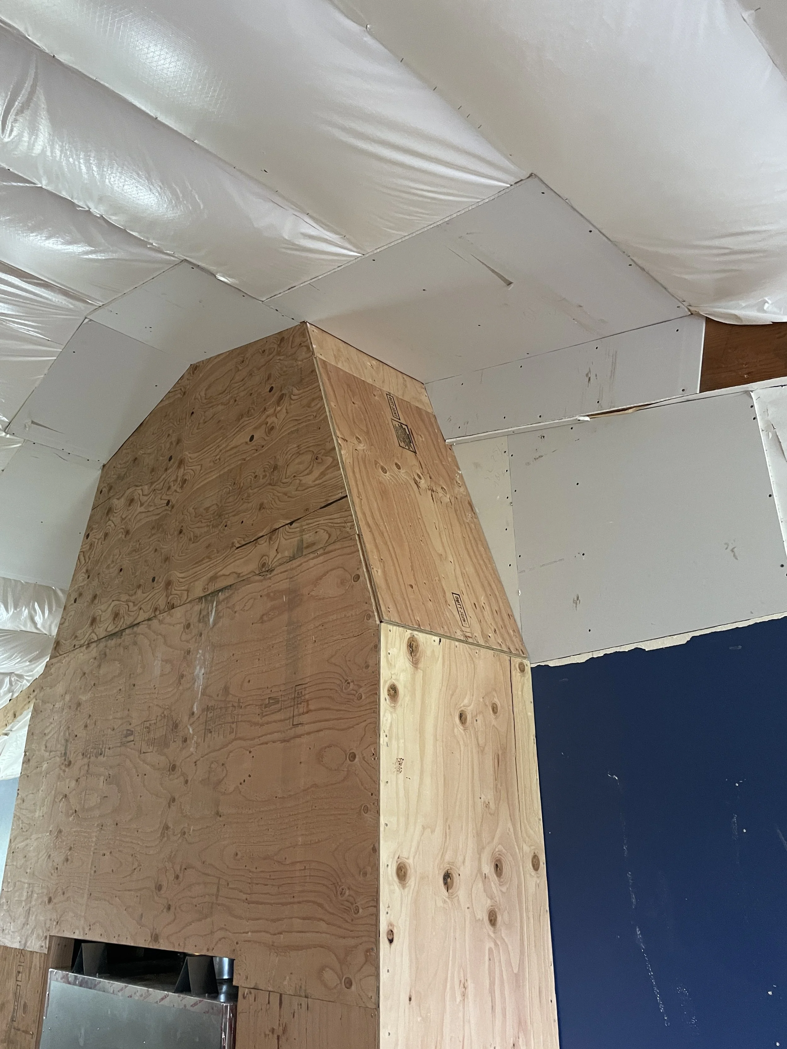 Construction area with wooden and drywall panels on the ceiling and wall, and shiny white insulation or vapor barrier covering the ceiling.