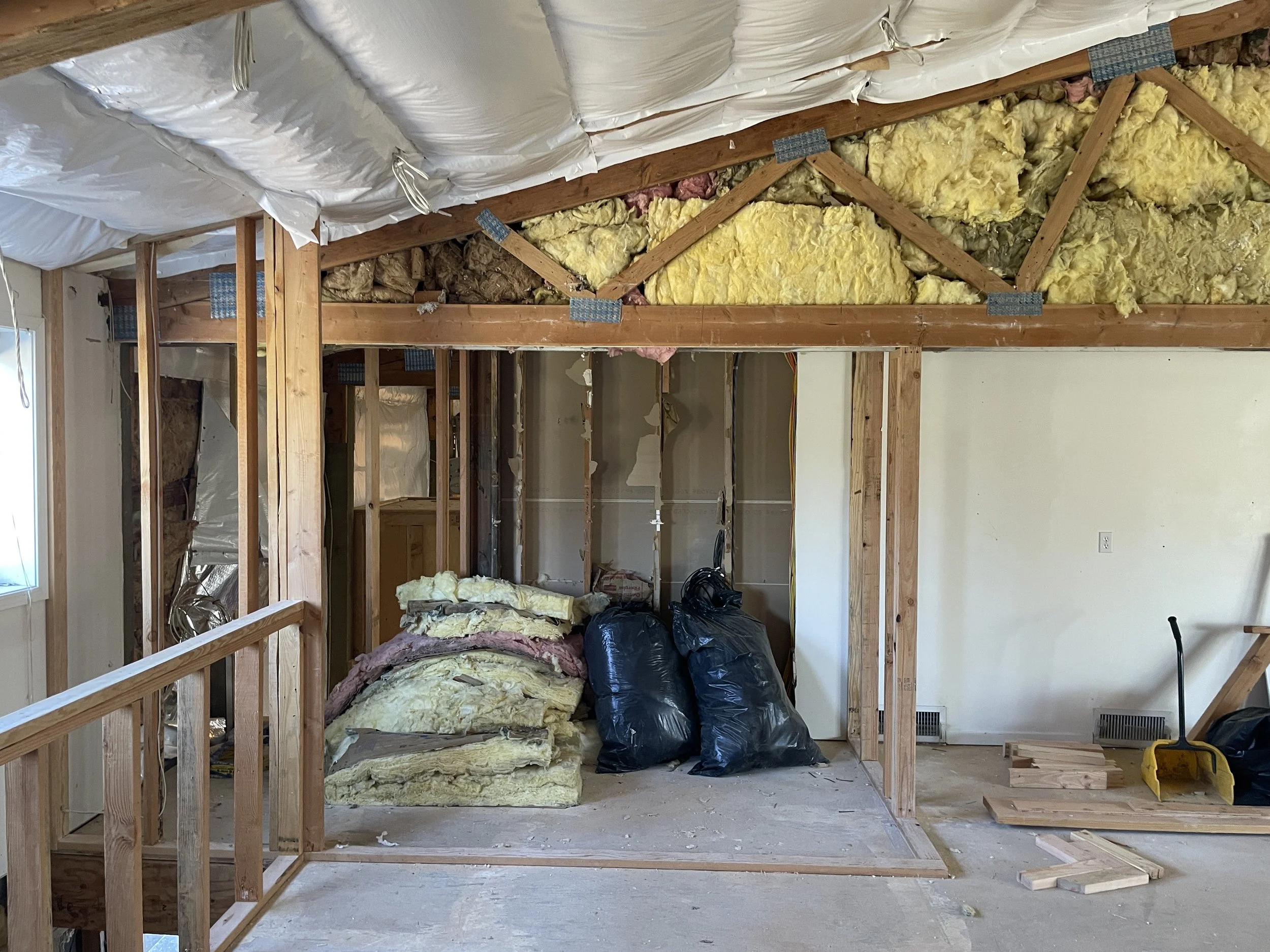 Interior view of a room under construction with wooden framing, insulation material, and plastic vapor barrier on the ceiling.