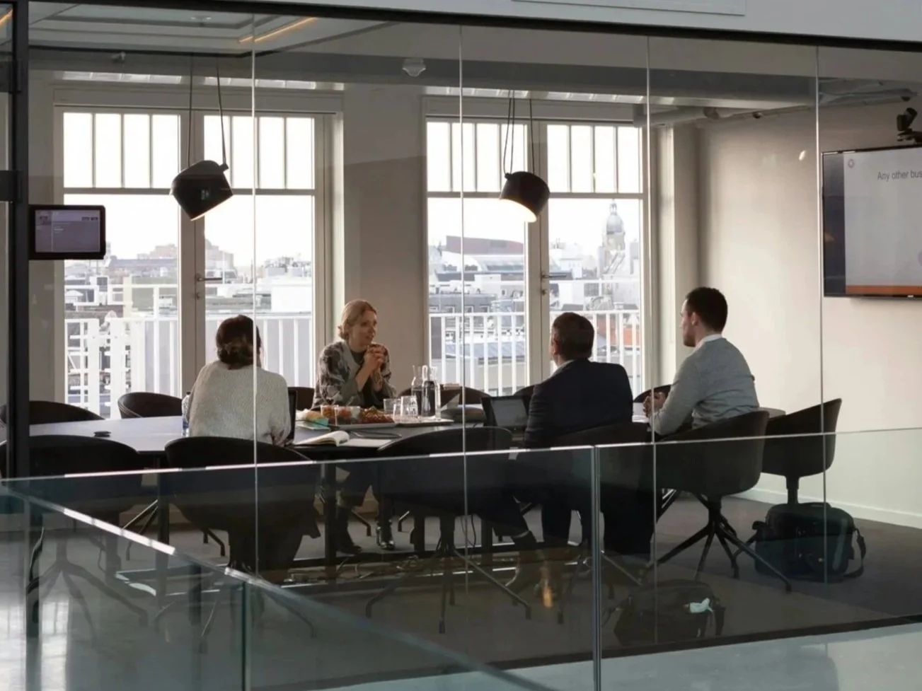 Four businesspeople having a meeting around a table in a conference room with large windows overlooking a cityscape.