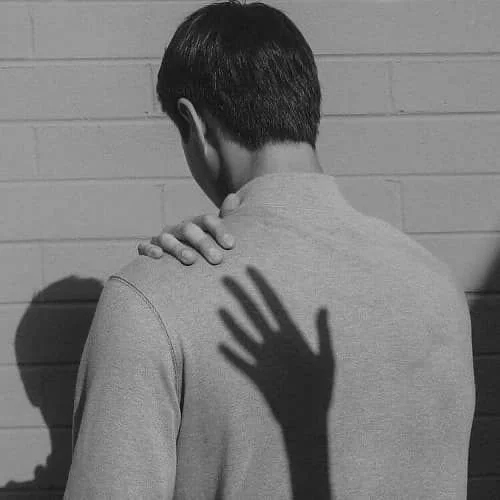 Una persona de espaldas, con sombra de una mano en la espalda, en blanco y negro.