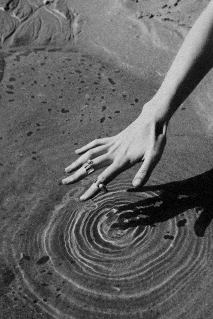 Mano tocando el agua en la orilla de la playa.