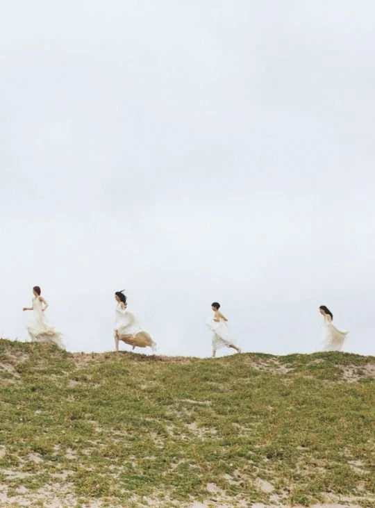 Cuatro personas corriendo por una colina cubierta de pasto, con un cielo despejado de fondo.