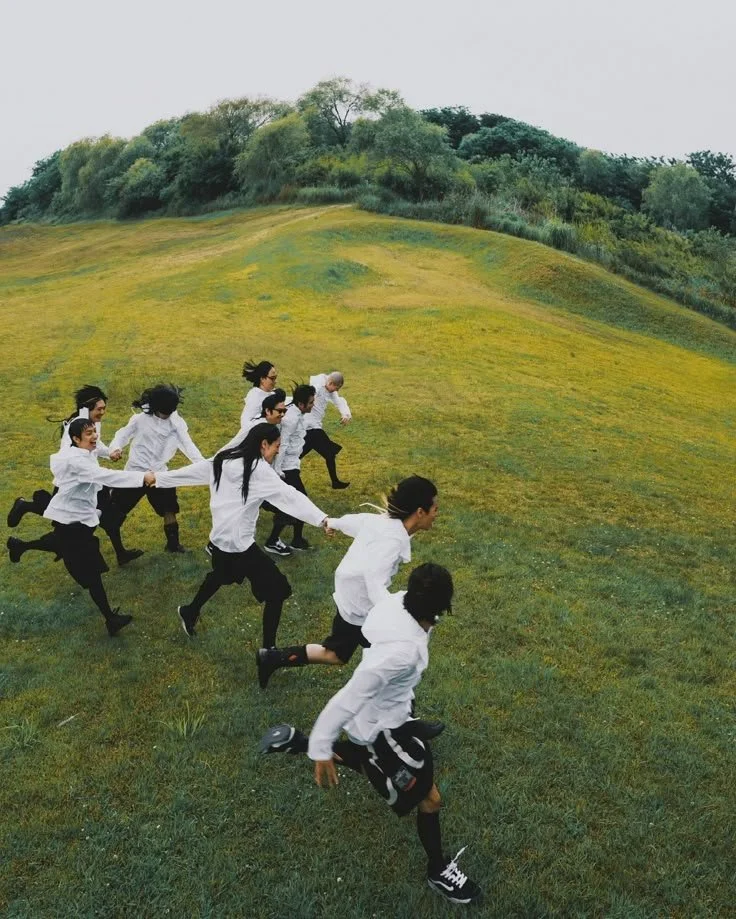 Niños con uniforme escolar corriendo cuesta arriba en un campo verde con árboles al fondo.