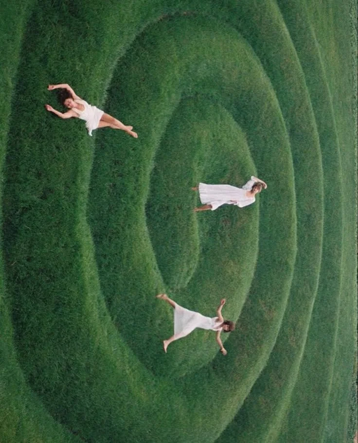 Tres personas en vestidos blancos en un campo de hierba cortada en forma de espiral