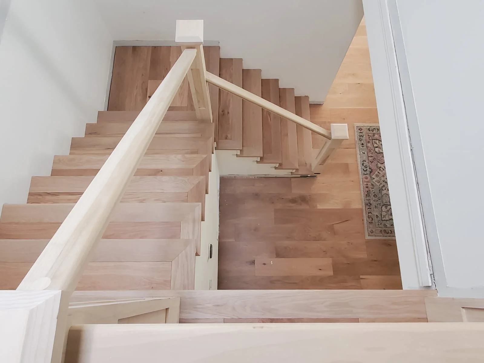 Interior staircase with wooden steps, handrail, and a small area of hardwood flooring visible at the bottom.