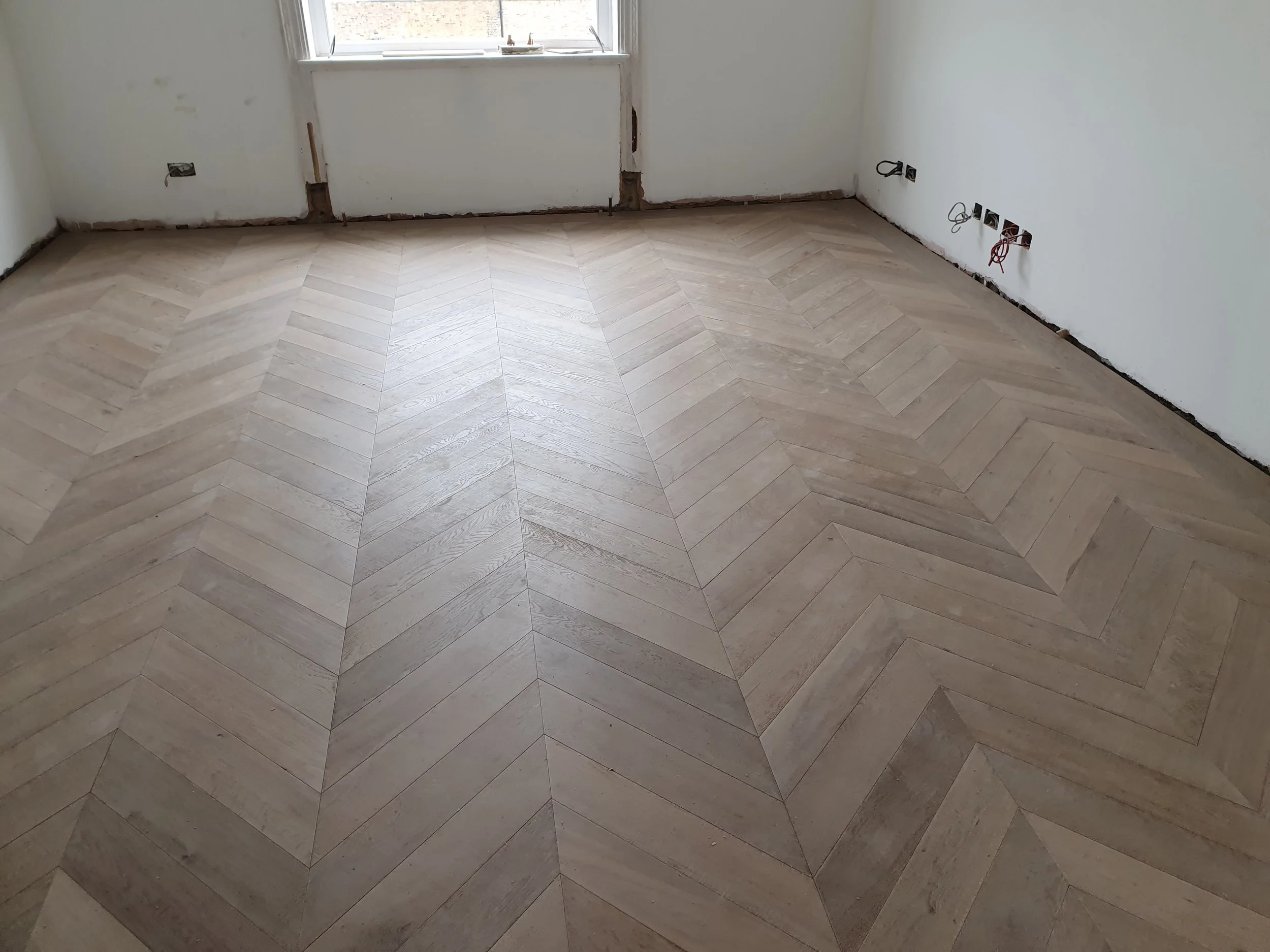 Room with partially finished wall and new wooden herringbone patterned floor.