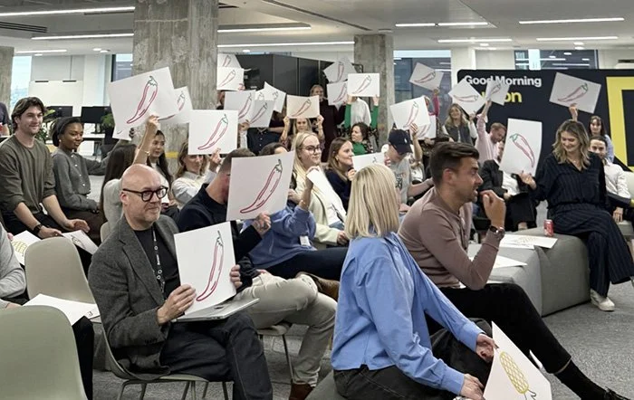 A group of people holding up cards in an office environment as they attend a creative presentation at Burson