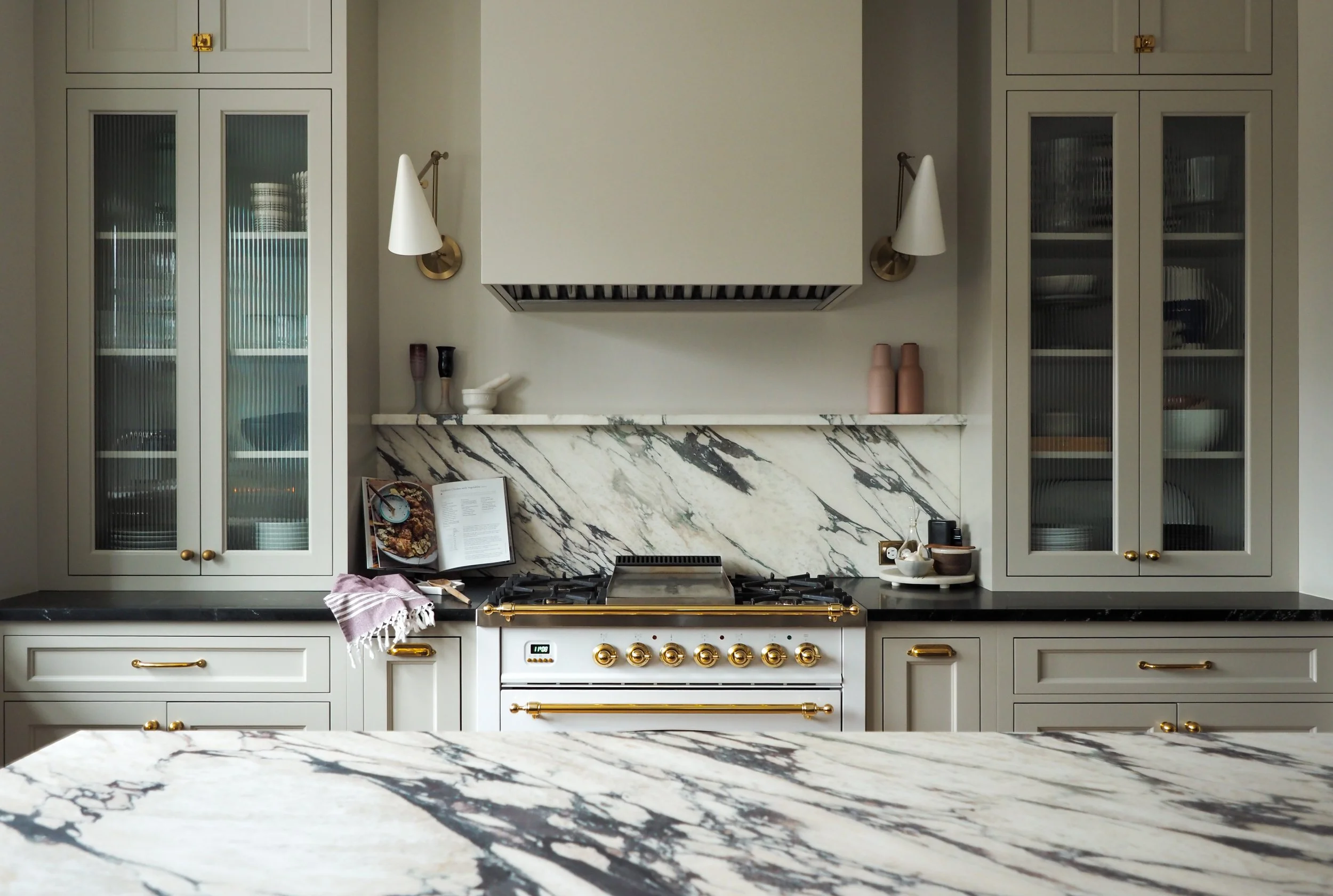 soft grey kitchen cabinetry with marble backsplash, brass hardware, and professional range — Studied Milieux interior design