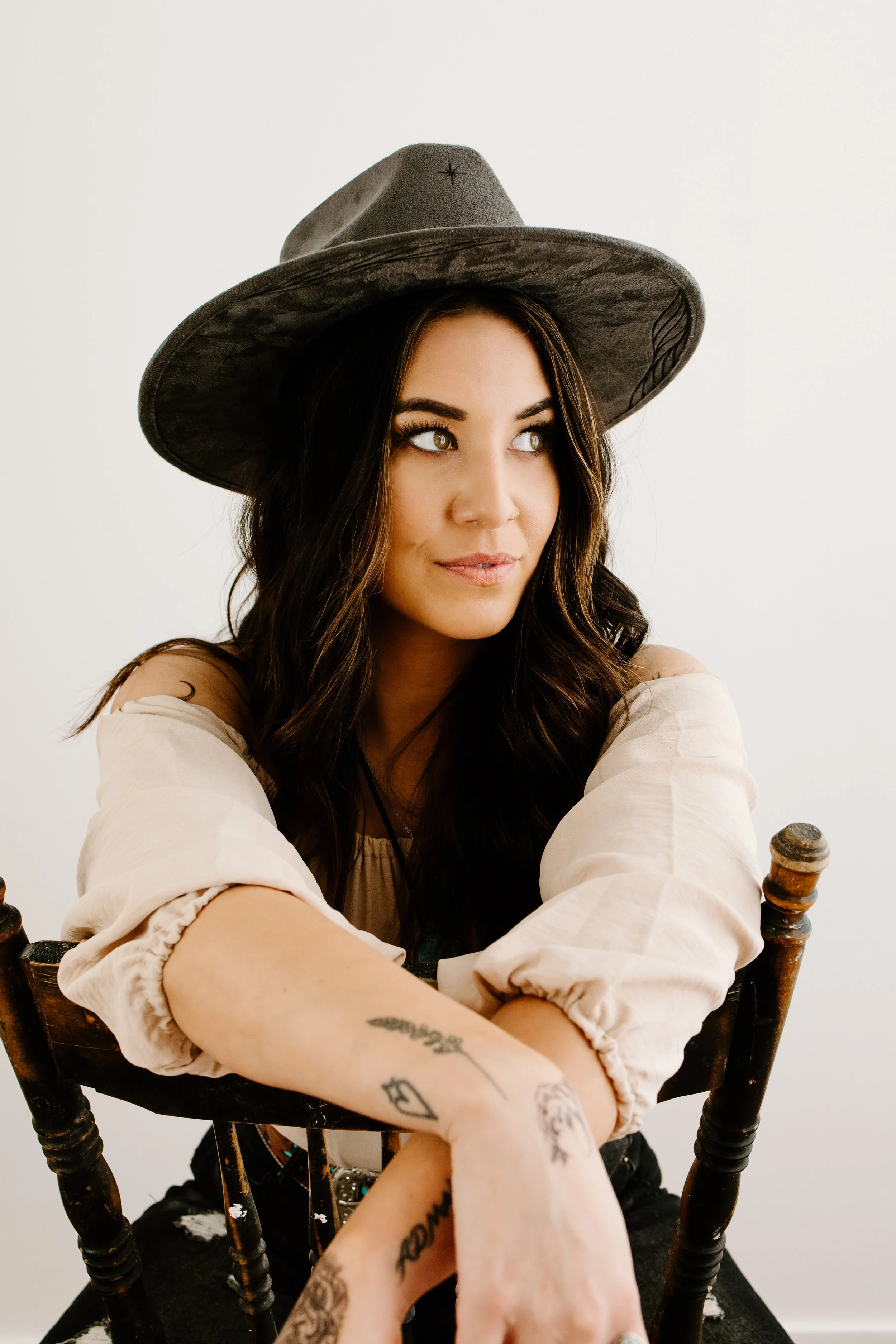 Woman with hat and tattoos sitting on a chair.