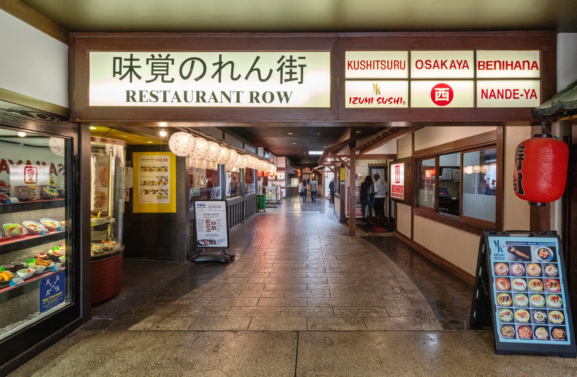 Indoor shopping mall corridor with restaurant signs, lanterns, and menus on display